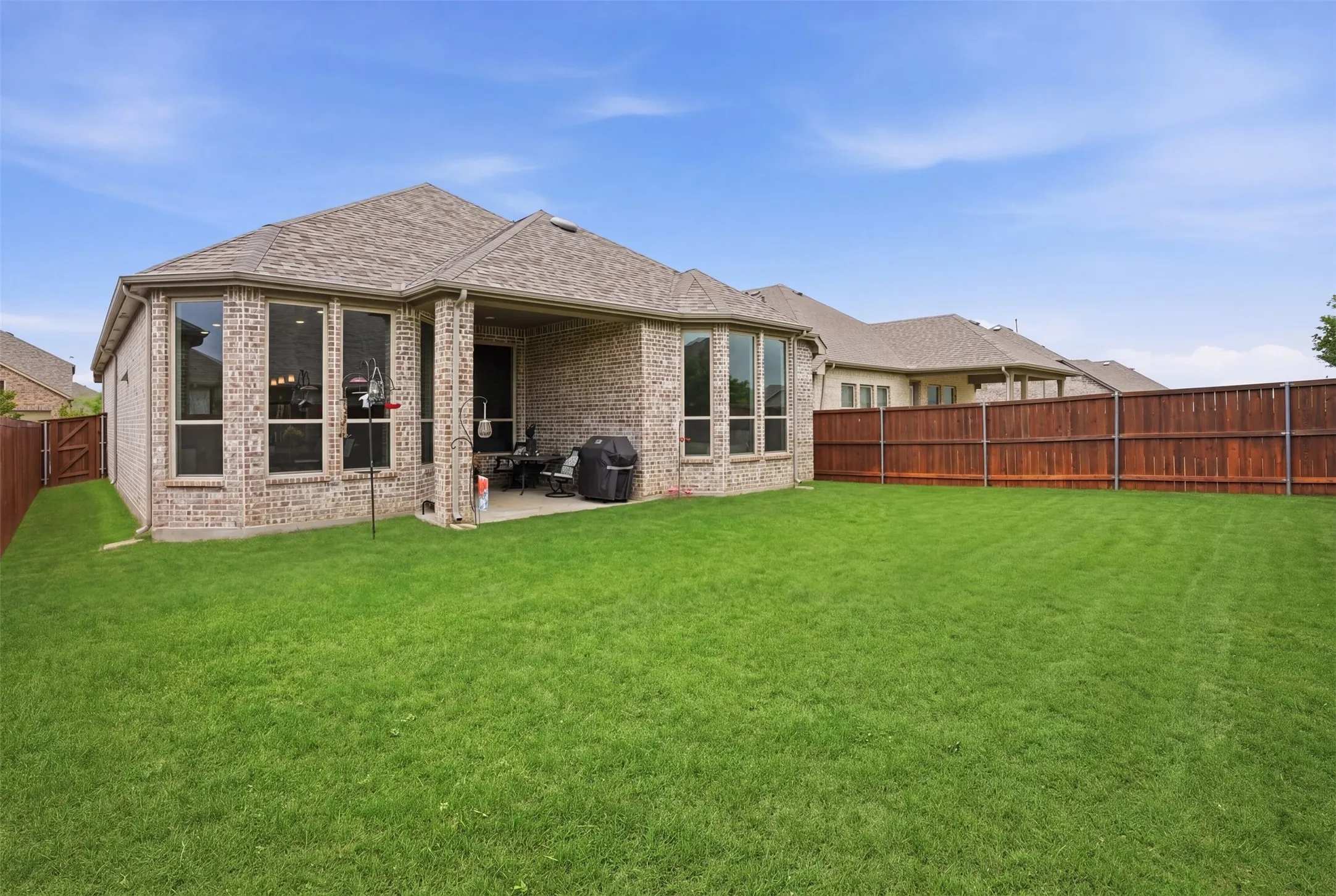 This property features an expansive green lawn, a covered patio area, and a privacy fence