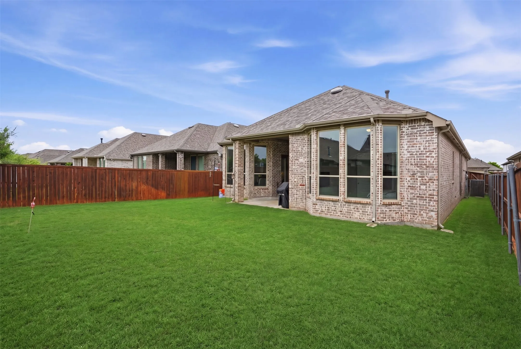 The property features an extensive green lawn, a brick exterior, and a fenced yard