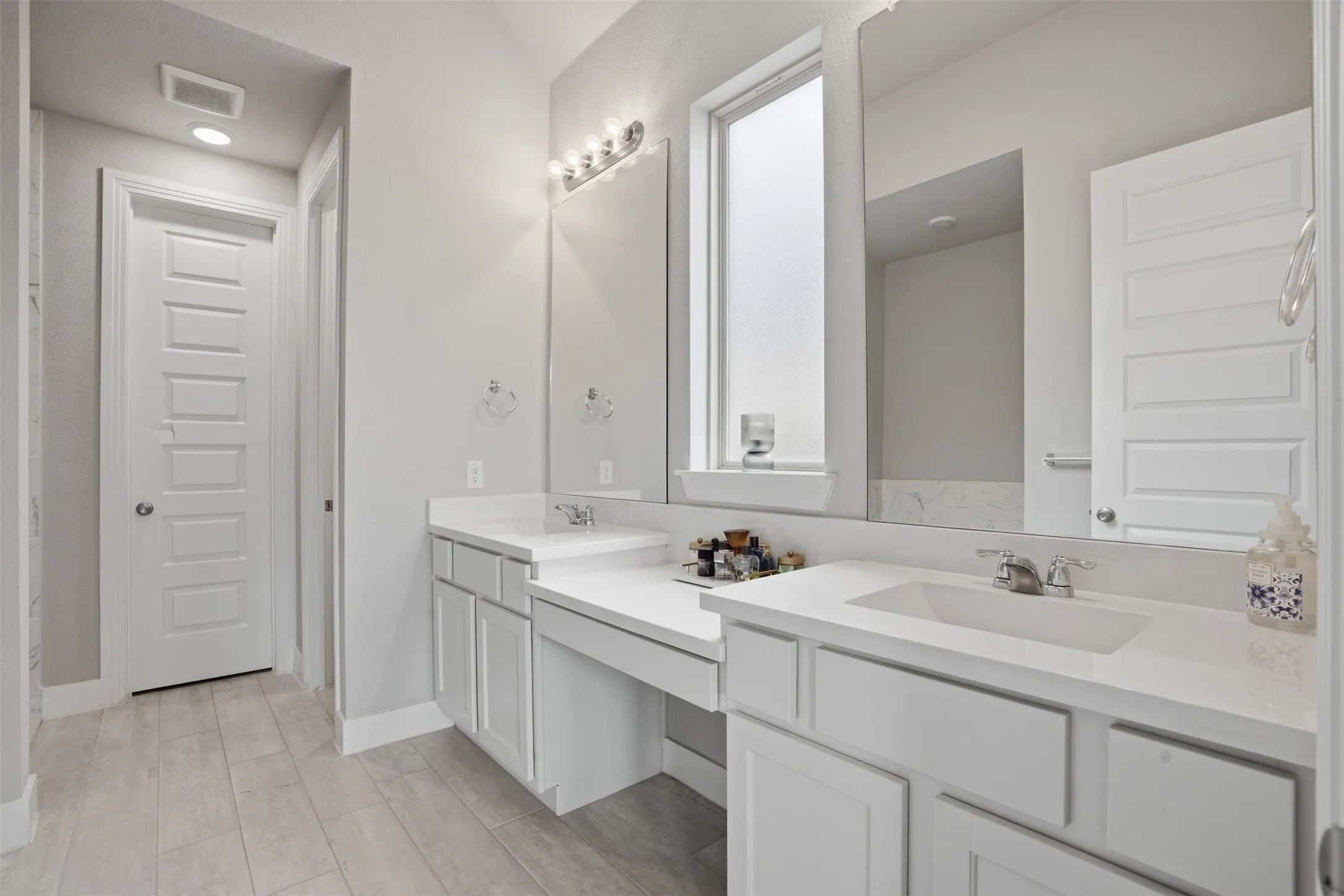 Bathroom featuring a dual vanity with white cabinetry, a built-in dressing table, and a large mirror