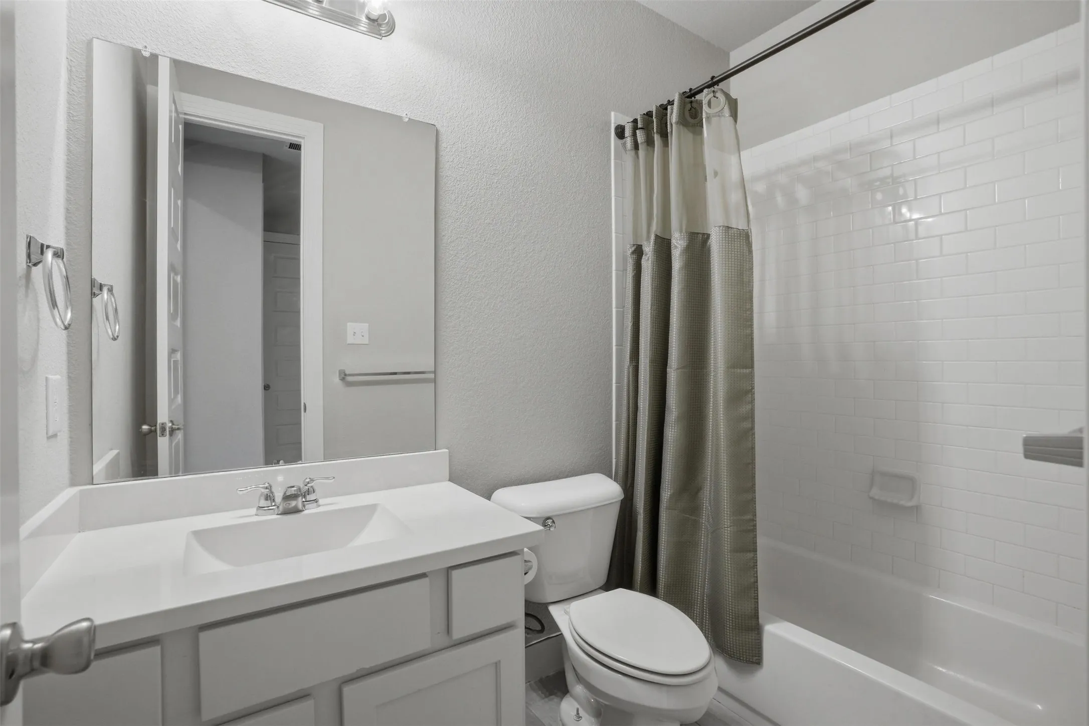 Bathroom featuring a vanity with an integrated sink and a large wall mirror, a toilet, and a bathtub with white subway tile surround