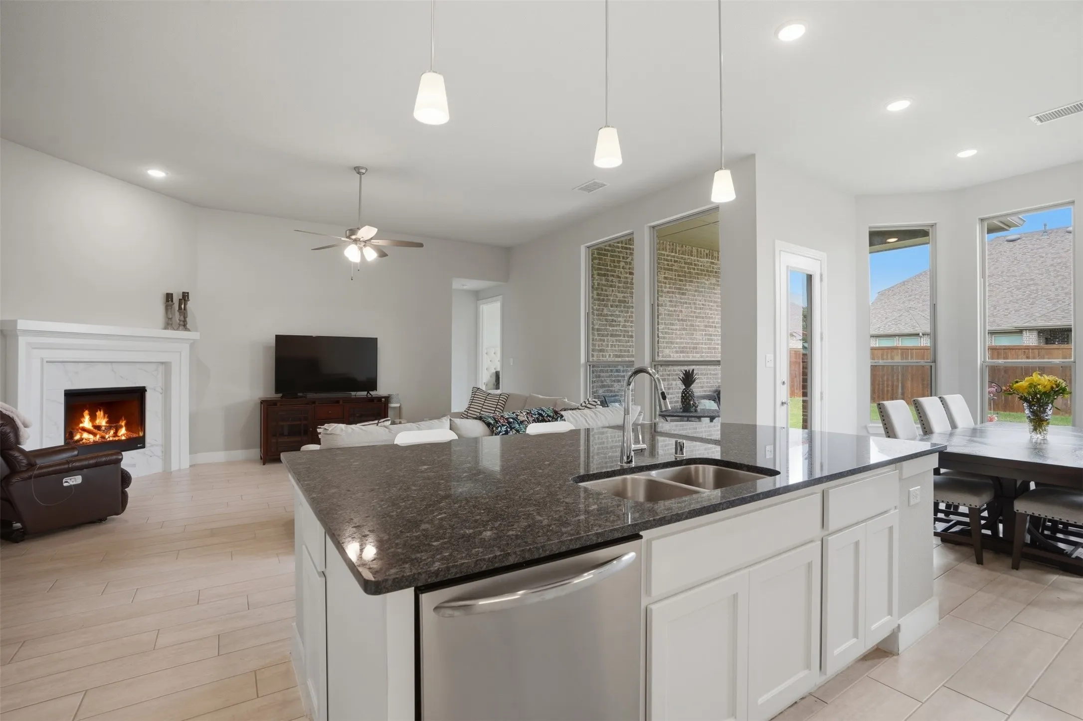 Open-concept living space featuring a kitchen island with a double sink and granite countertop, a dining area with large windows, and a living room with a fireplace