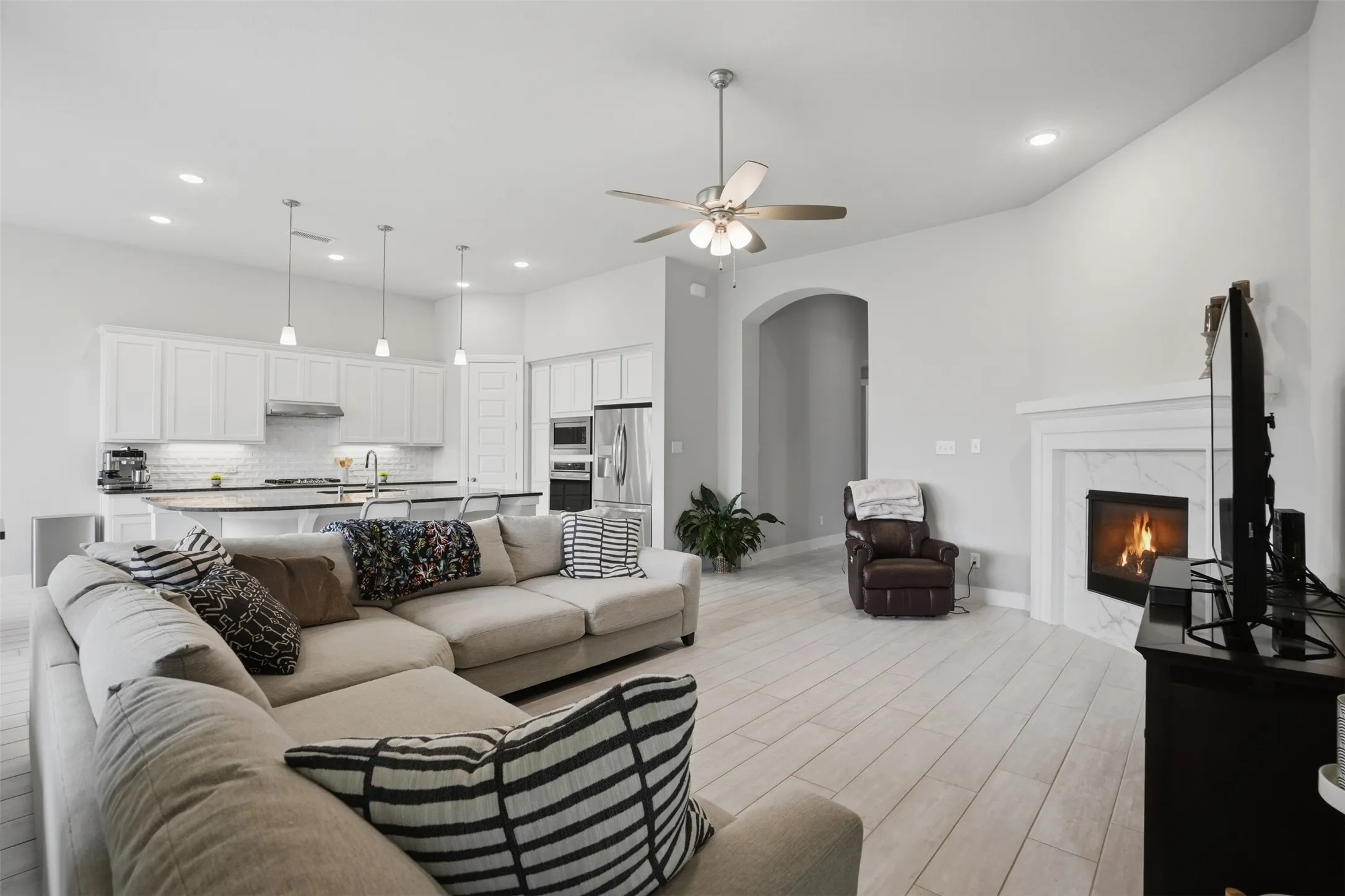 The main living area features light-colored flooring, a fireplace with a white mantel, and a ceiling fan