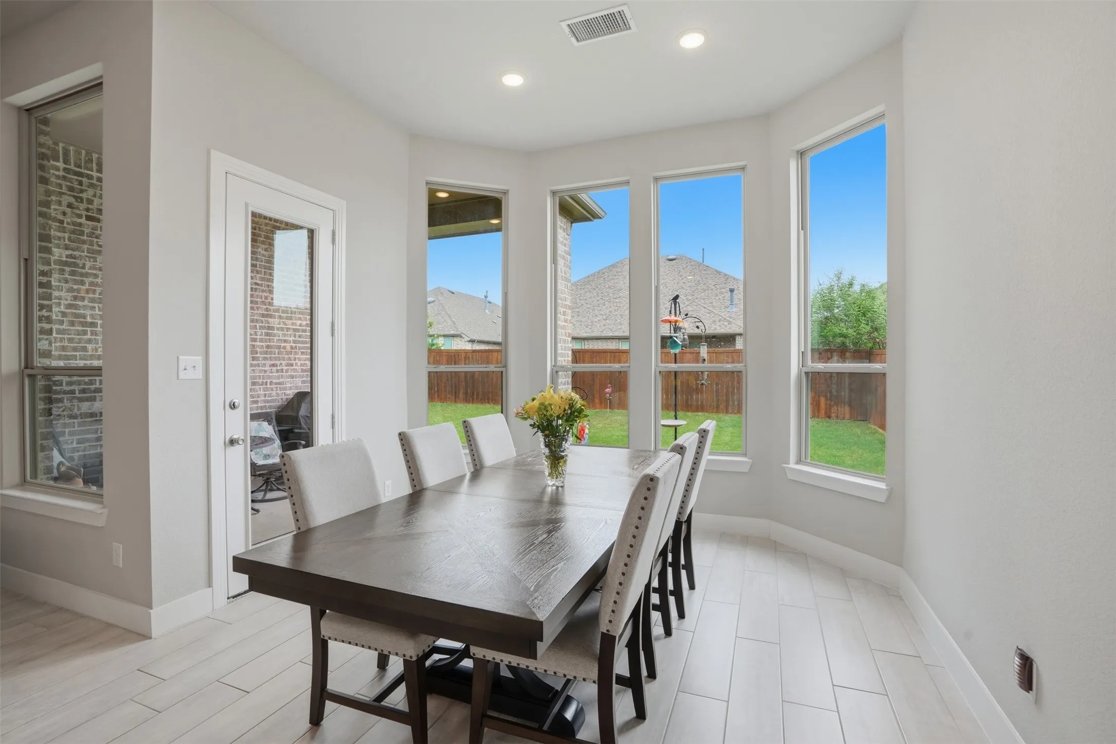 Bright dining area featuring light-colored flooring, recessed lighting, and a bay window with views of the backyard