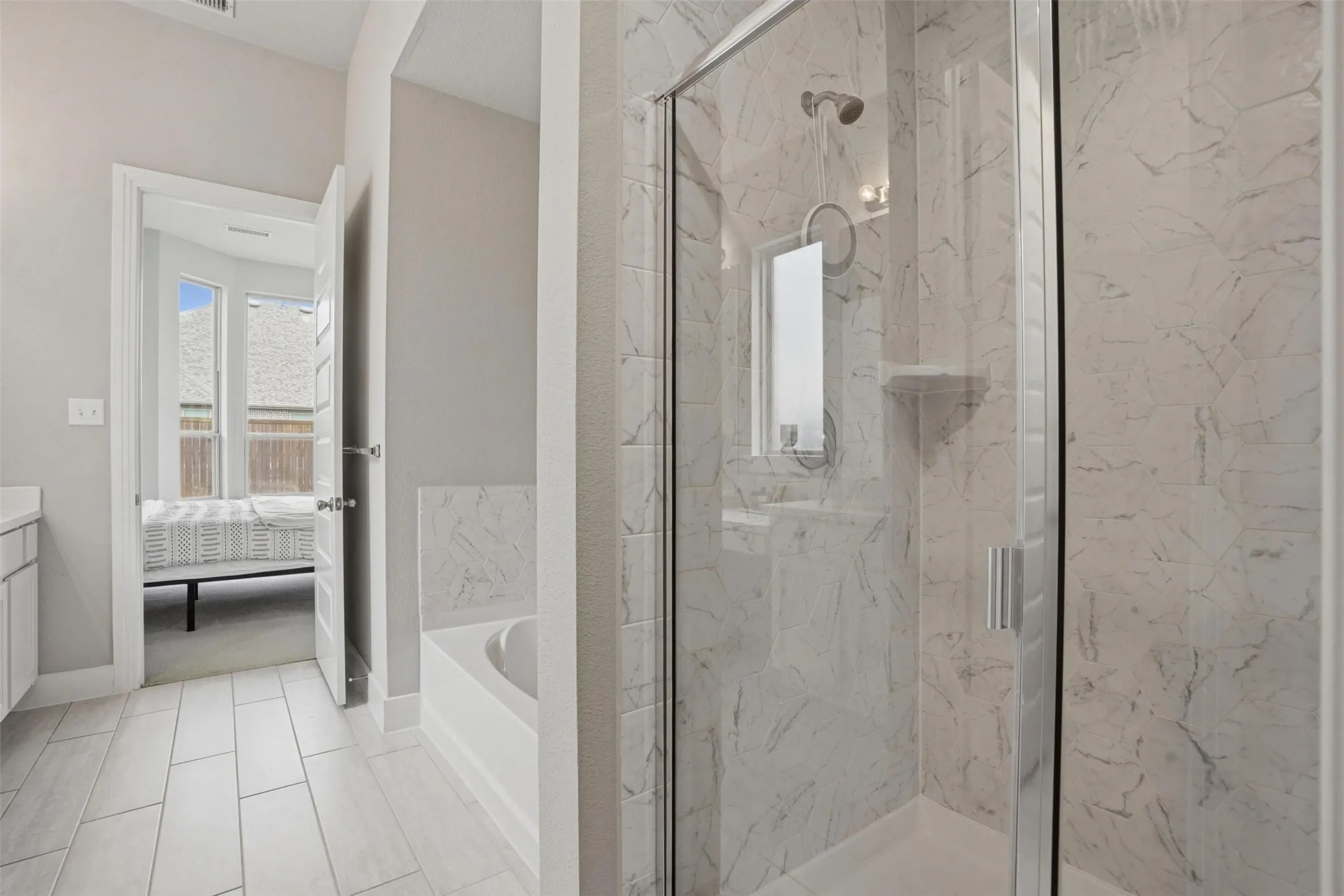 The bathroom features a spacious glass-enclosed shower with white marble-patterned tiling, a built-in shelf, and a showerhead