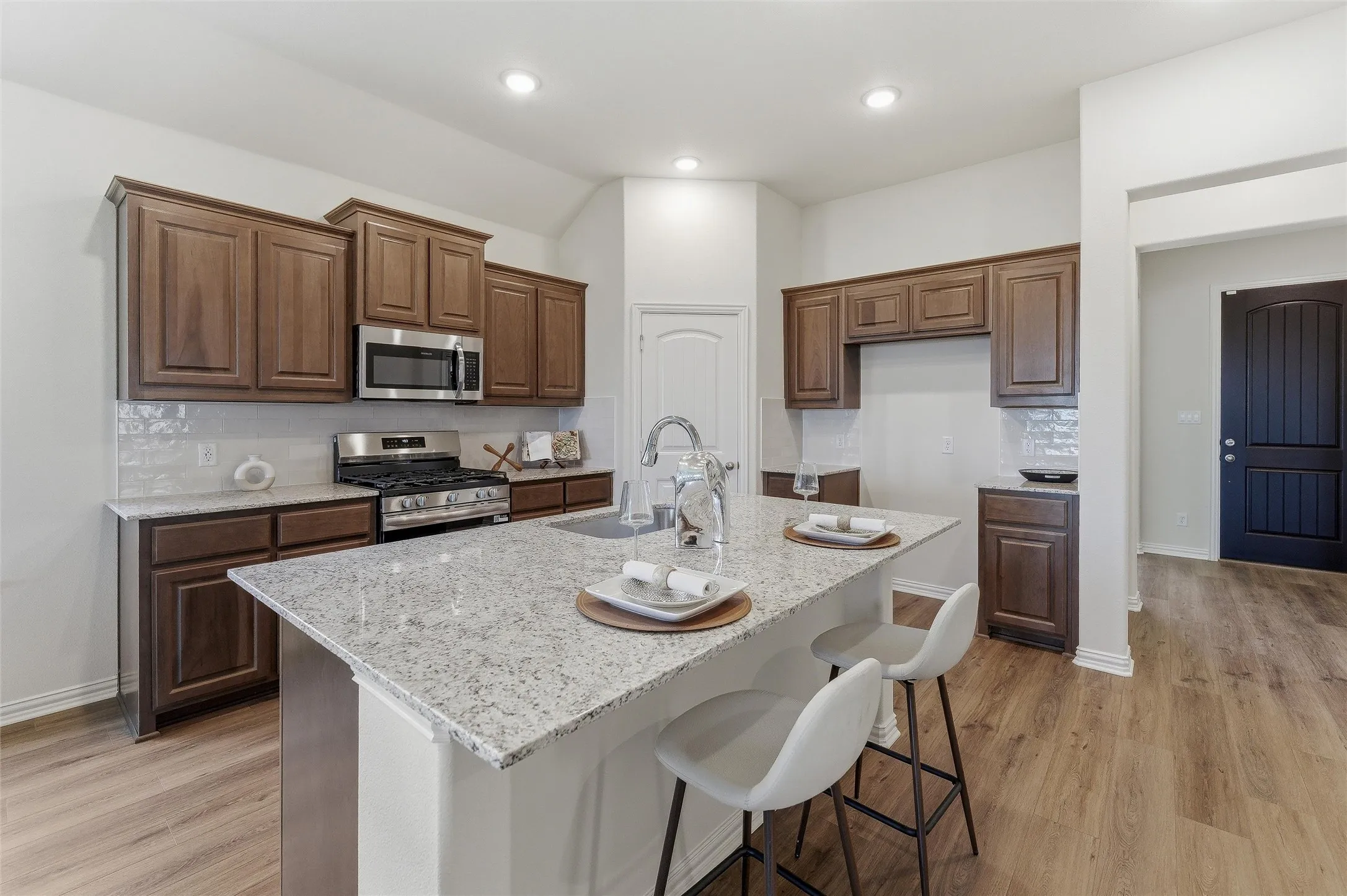 Kitchen featuring a large central island with seating, stainless steel appliances, dark wood cabinetry, white subway tile backsplash, and light wood-finish flooring