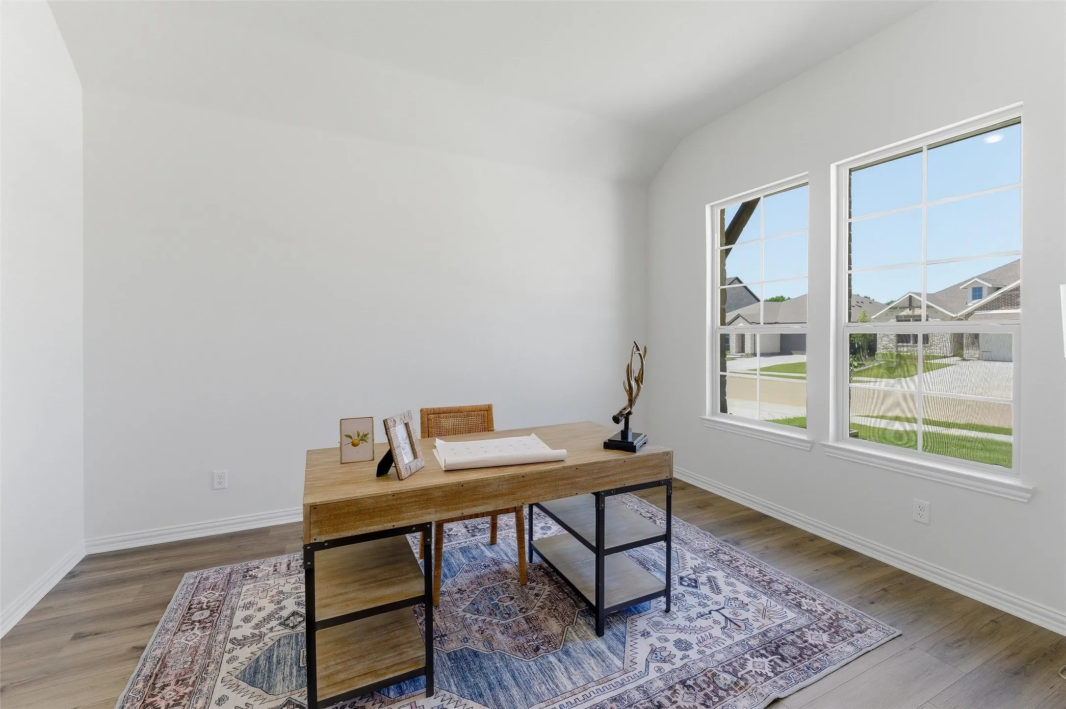 Room featuring two large windows with grid muntins, wood-finish flooring, white baseboards, and vaulted ceilings