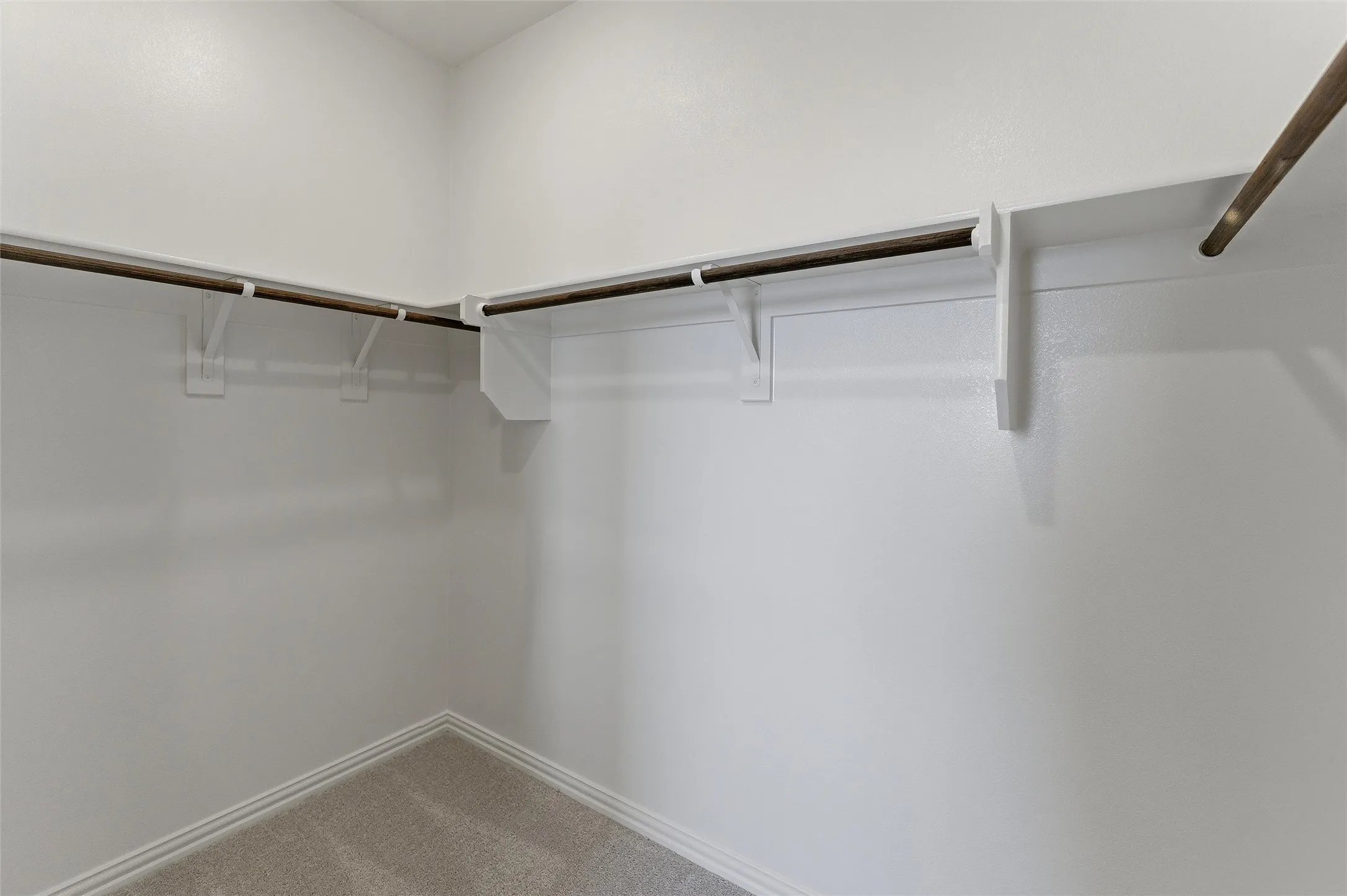Walk-in closet featuring light-toned carpeting, white baseboards, and built-in white shelving with wood-finish hanging rods