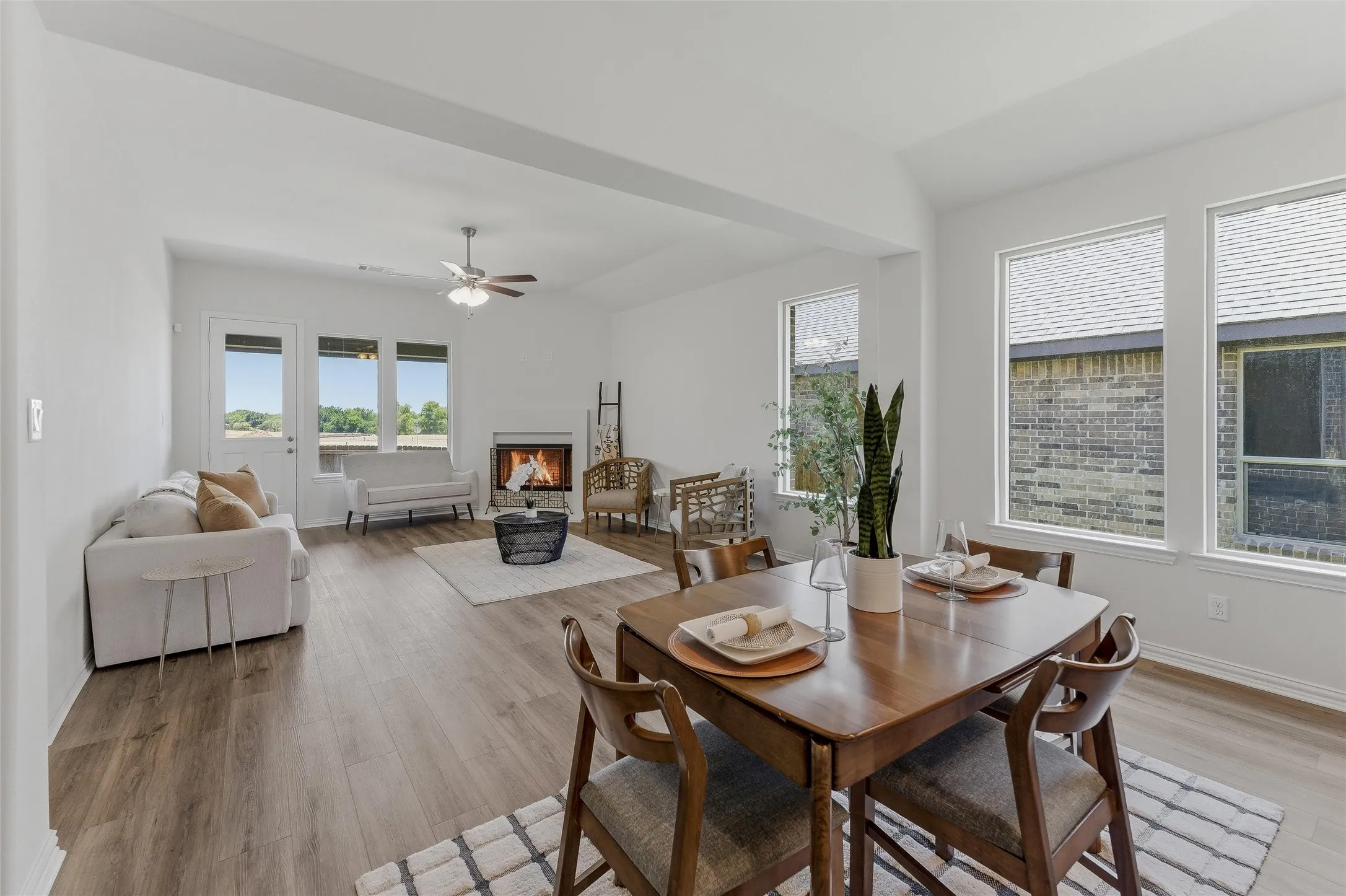 Open-concept living and dining area featuring wood-finish flooring, a white brick fireplace, and multiple large windows