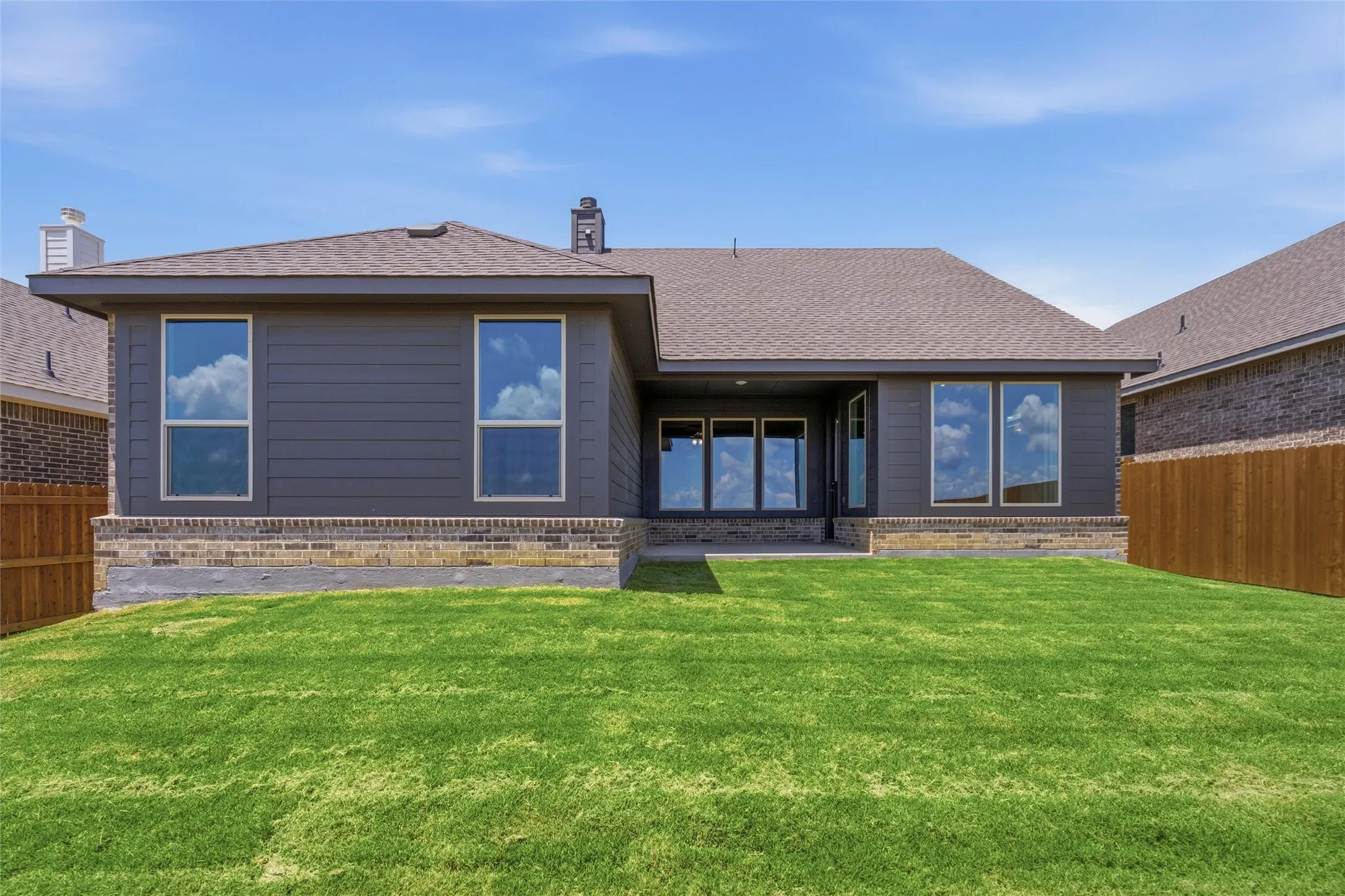 Expansive green lawn with a contemporary house exterior featuring dark siding, a dark shingle roof, and a brick base