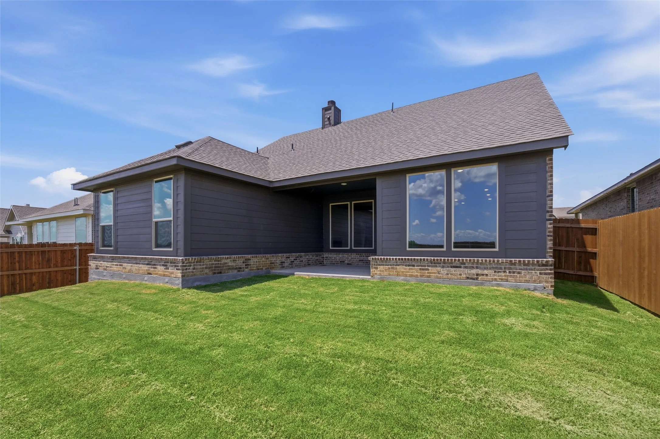 Rear exterior featuring dark gray siding, brick wainscoting, and large windows