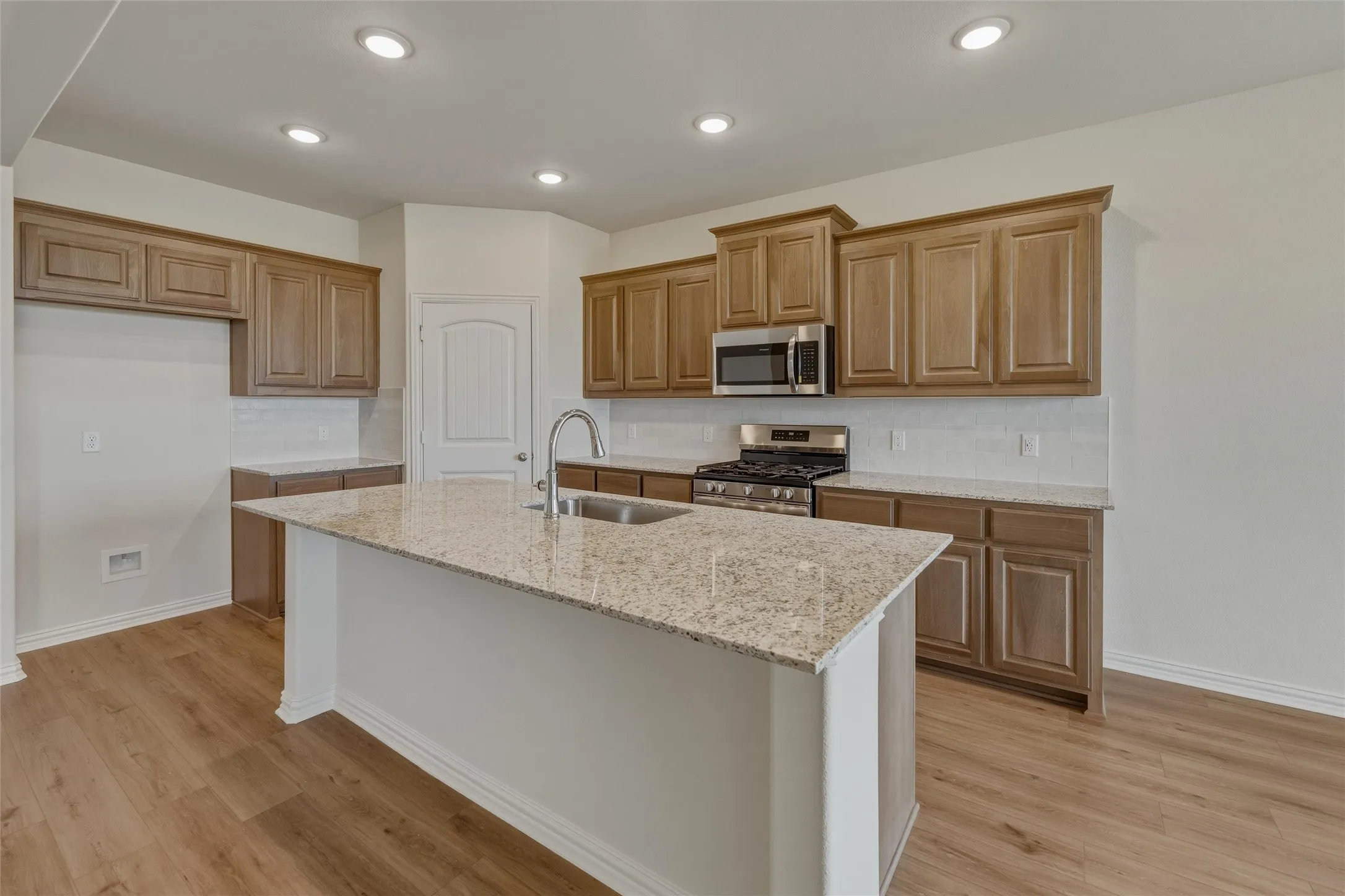 Kitchen featuring a large central island with a double basin sink, granite countertops, wood-finish flooring, recessed lighting, and stainless steel appliances