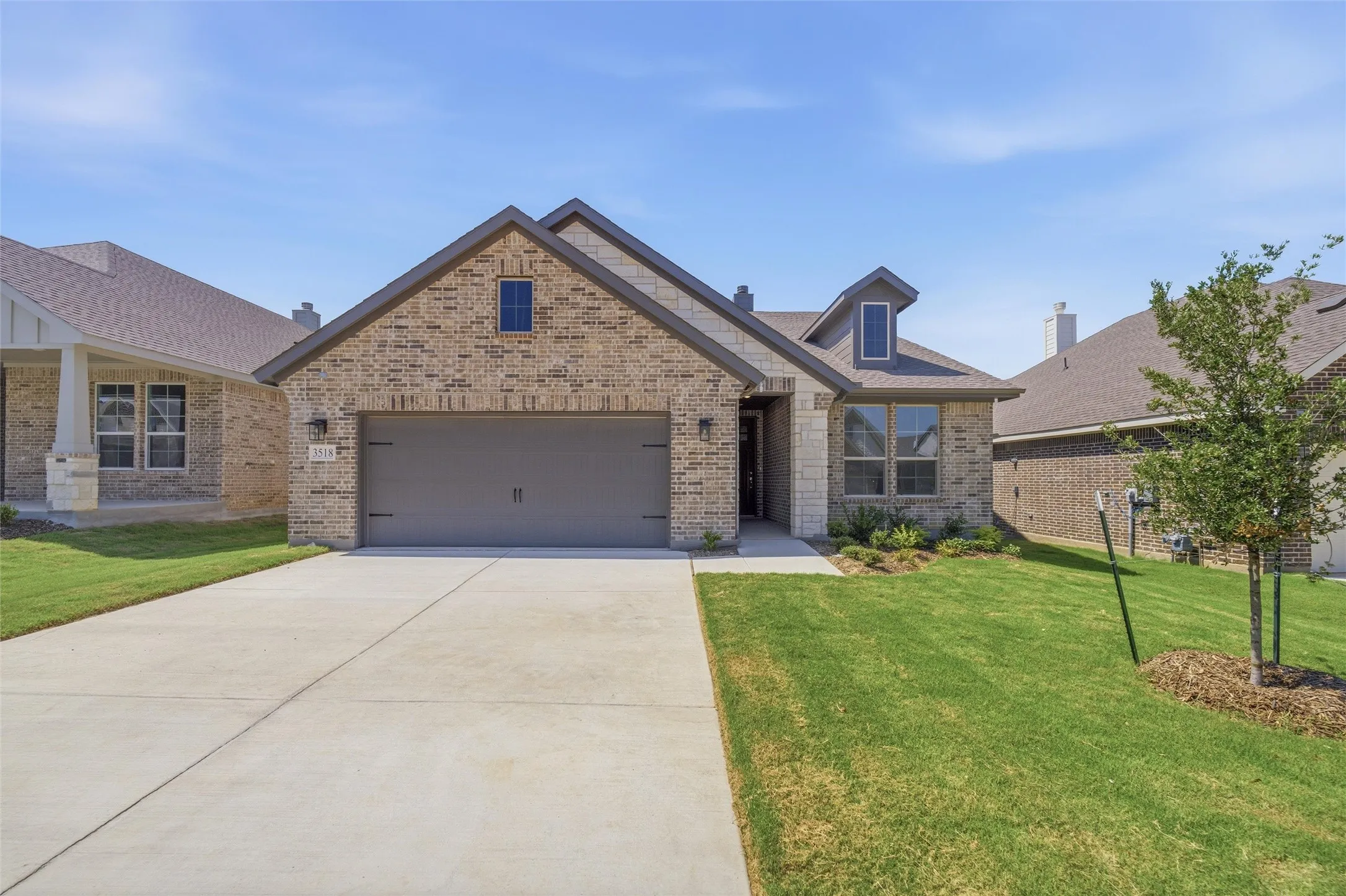 Brick and stone facade residence featuring an attached two-car garage, dormer windows, and a concrete driveway
