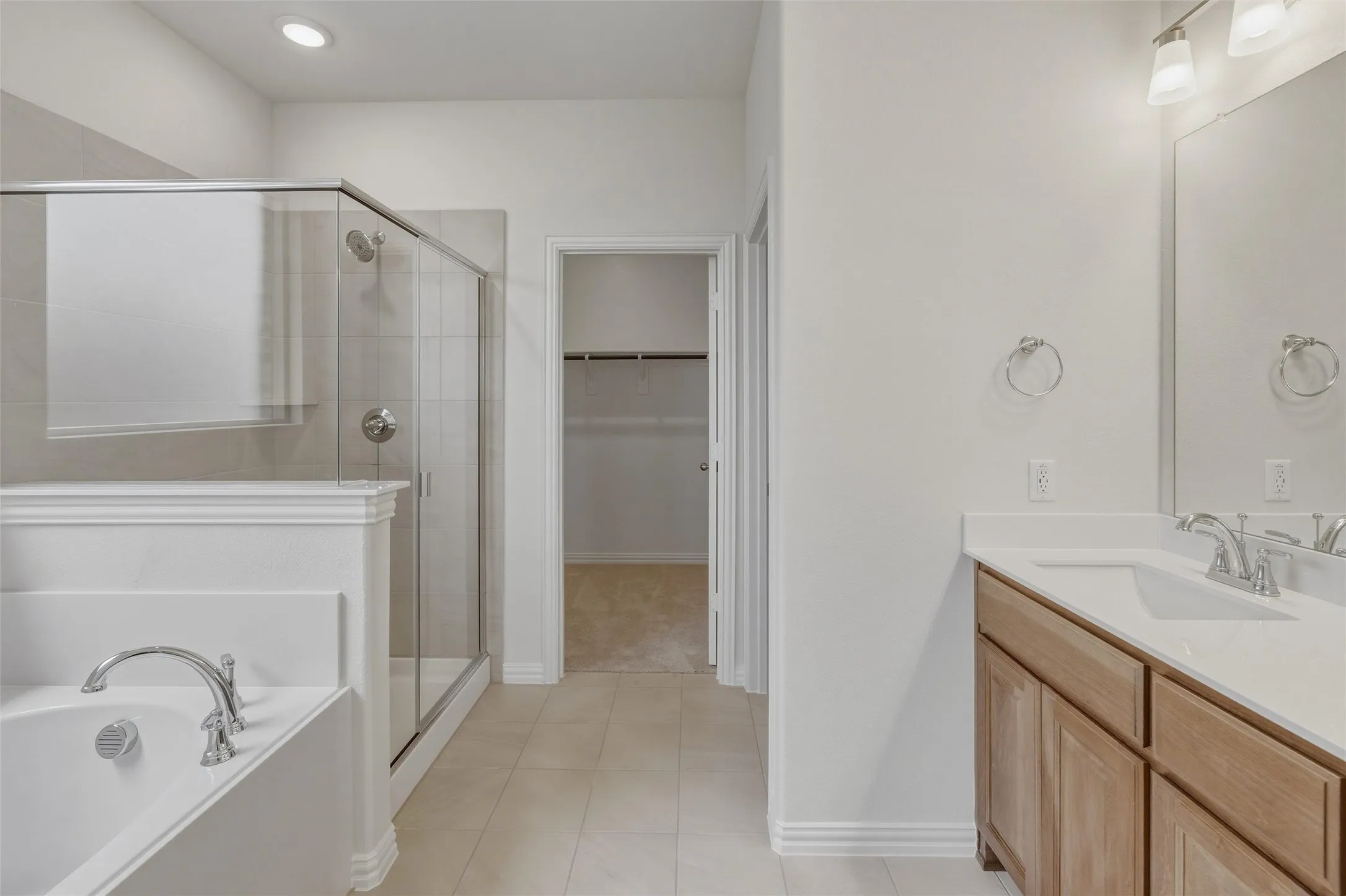 Bathroom featuring a frameless glass shower enclosure, a separate built-in soaking tub with chrome fixtures, a wood-finish vanity with a white countertop and integrated sink, and recessed lighting