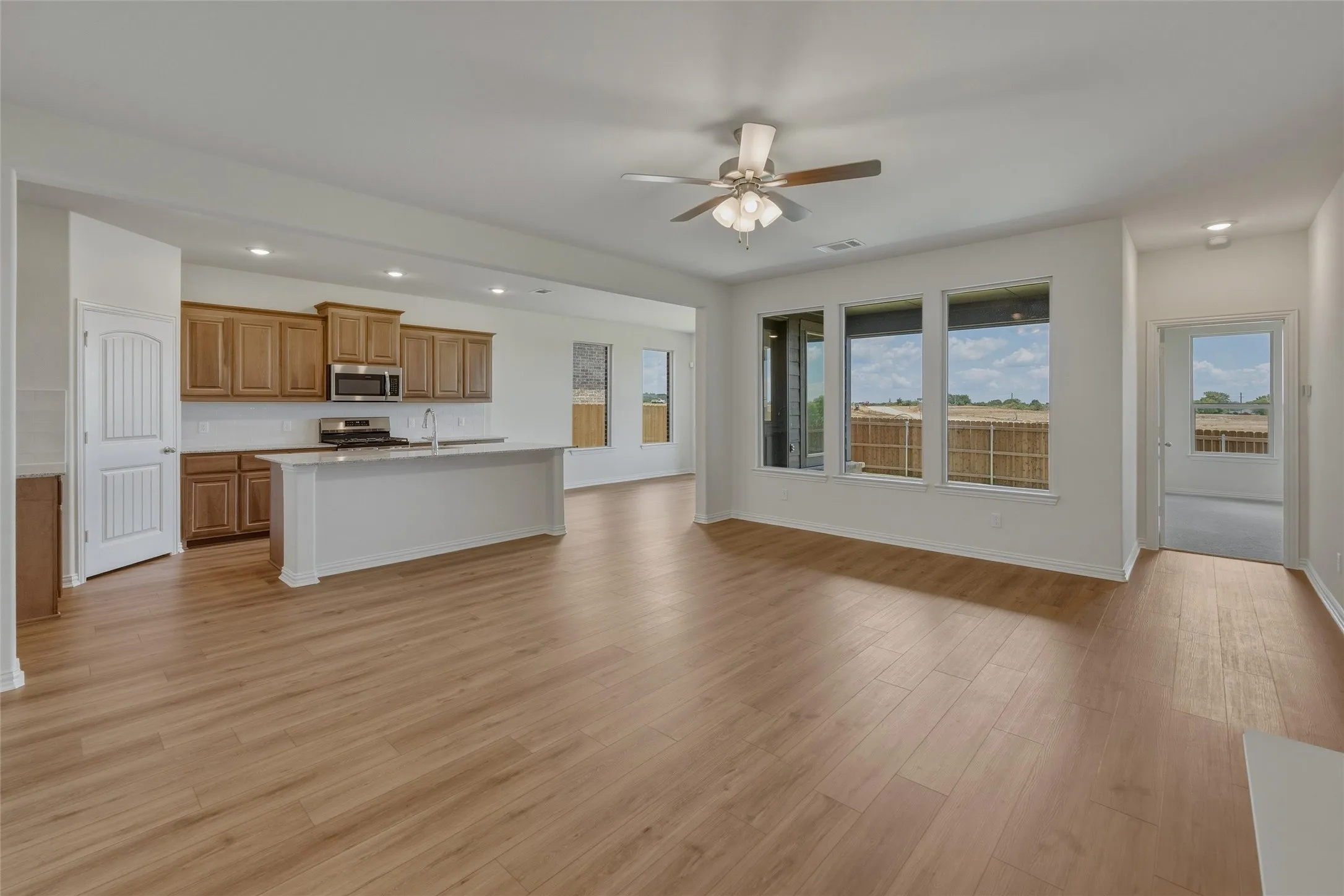 Open-concept living area with wood-finish flooring, a contemporary ceiling fan, and multiple large windows