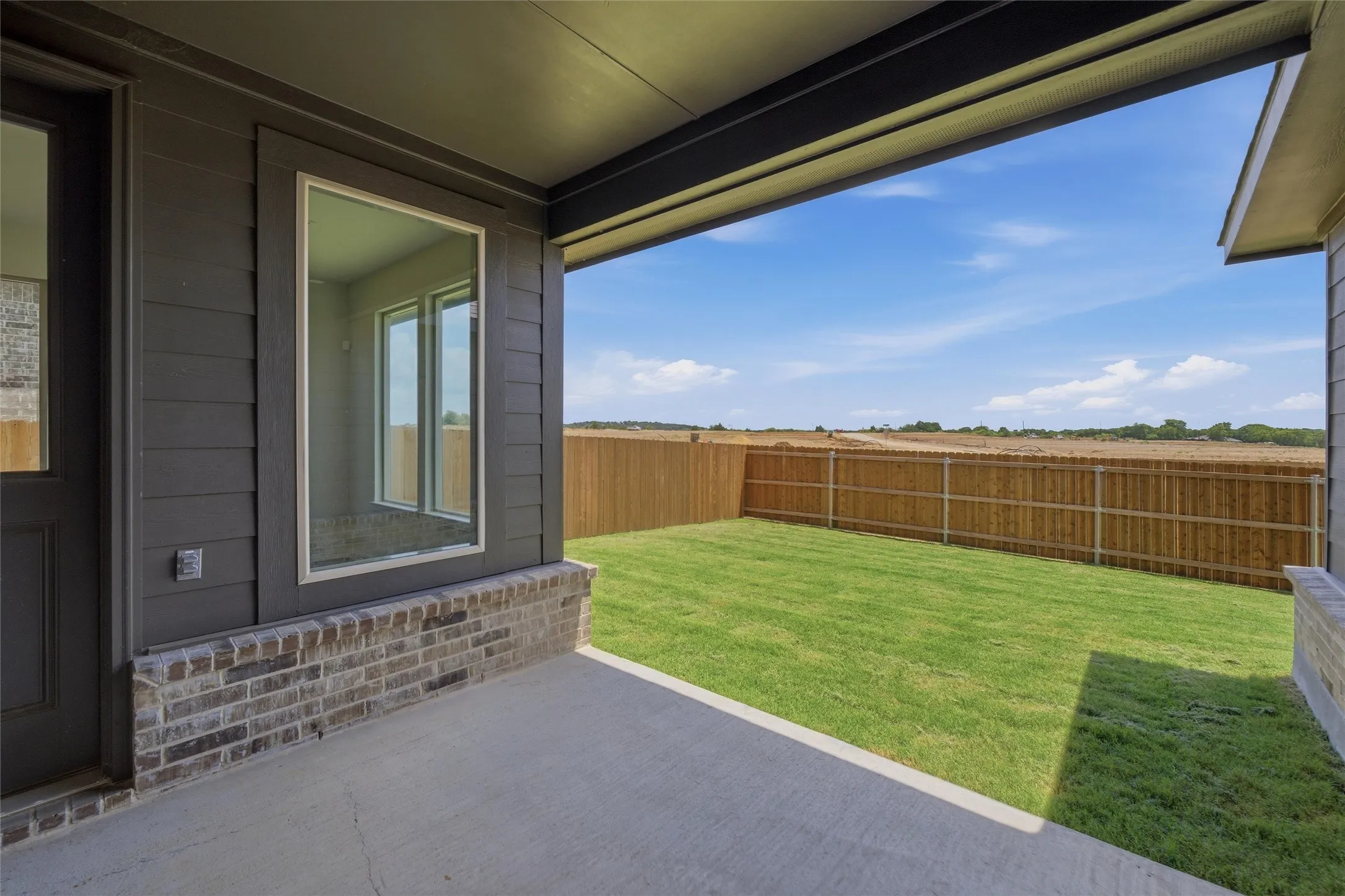 Concrete patio featuring a dark wood-finish door, large window with white trim, and a brick facade