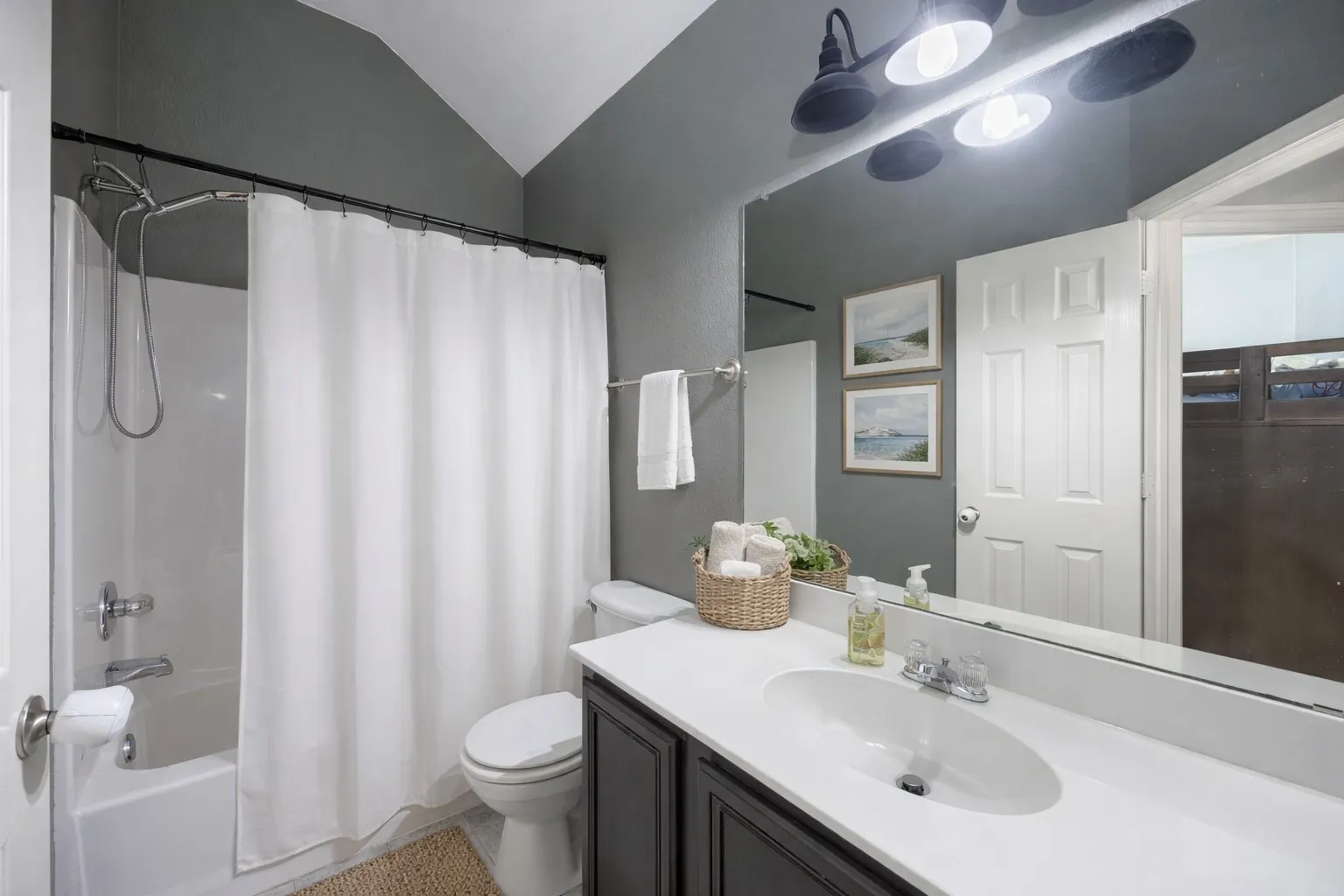 The bathroom features a vanity with a white countertop and a single basin sink, a large mirror, and a bathtub with a shower and white shower curtain