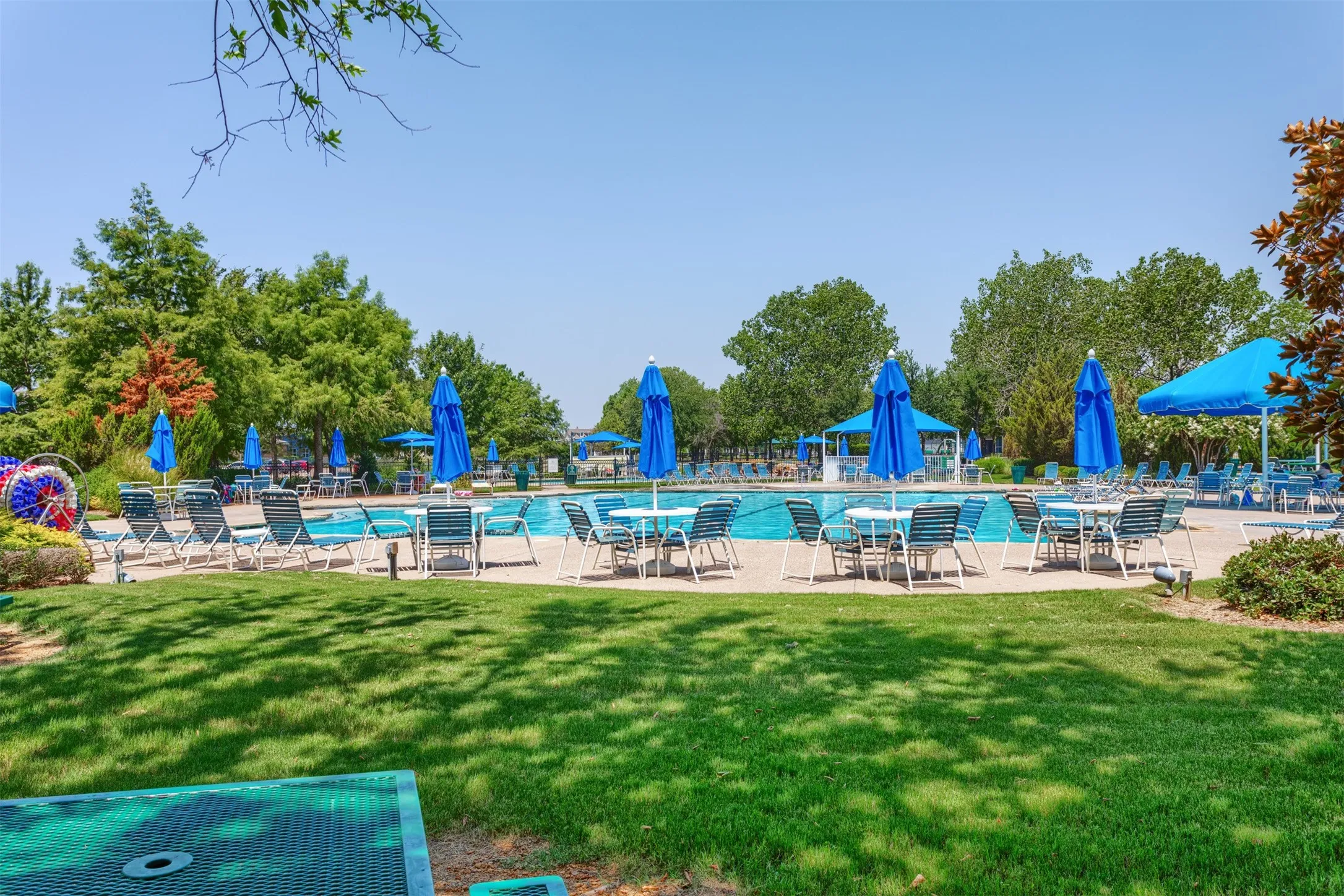 The property features an outdoor swimming pool area with numerous lounge chairs, tables, and blue umbrellas, set within a landscaped grassy expanse