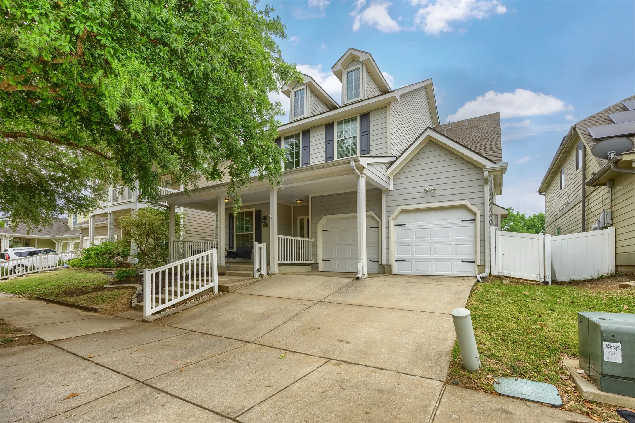 The property features a multi-story exterior with light-colored siding, dormer windows, and two garage doors