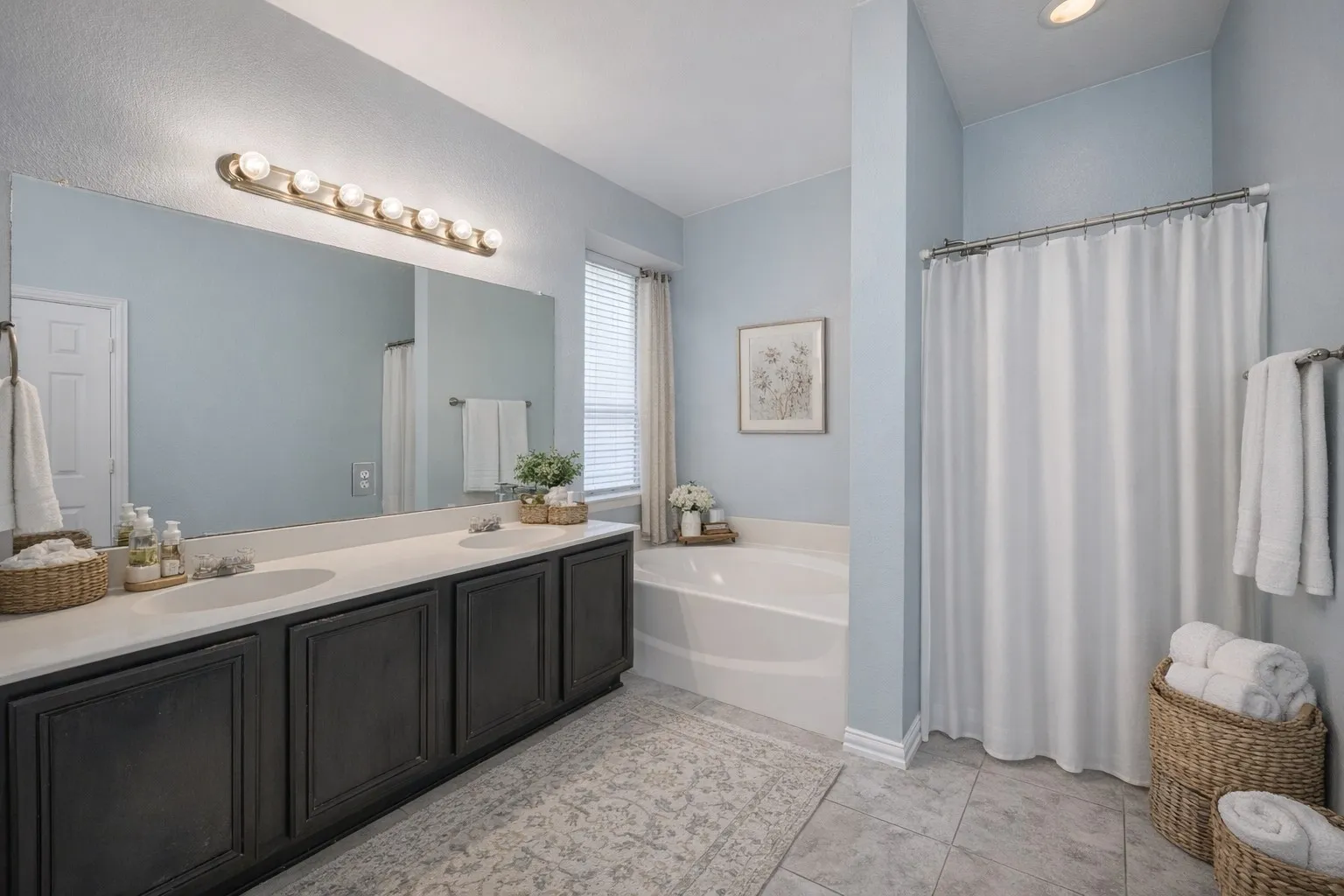 Bathroom featuring a double vanity with dark cabinetry, a large mirror, and an integrated bathtub