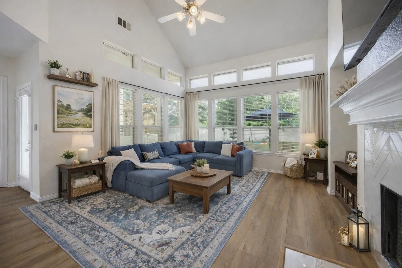 Living room featuring vaulted ceilings, hardwood floors, a ceiling fan, and large windows providing abundant natural light