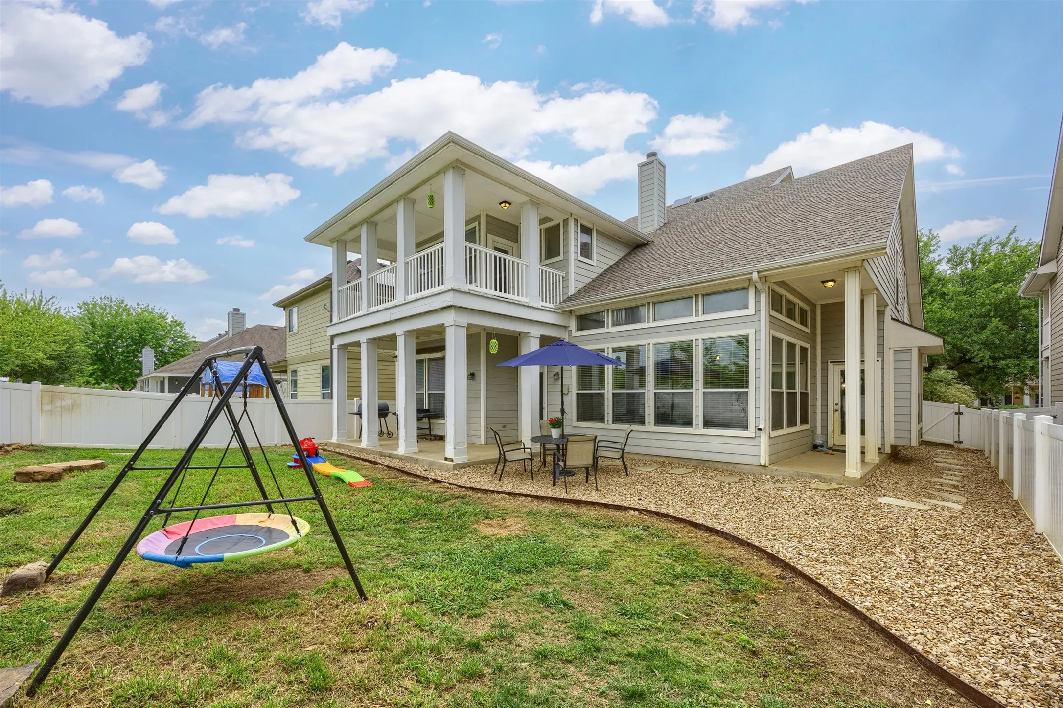 The property features a spacious backyard with a lawn and a gravel path, a covered patio with outdoor seating, and a sunroom with large windows