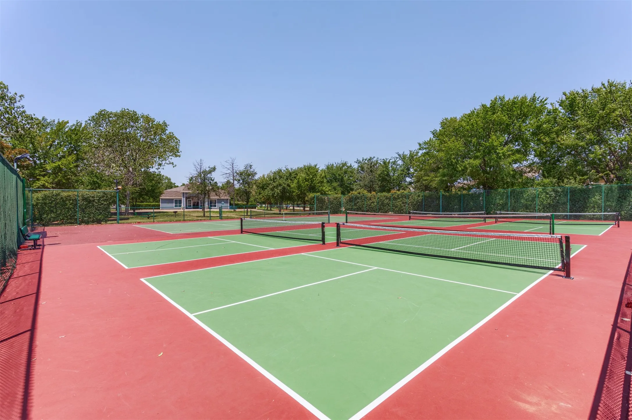 The property features outdoor courts with a red and green surface, complete with nets, and surrounded by fencing
