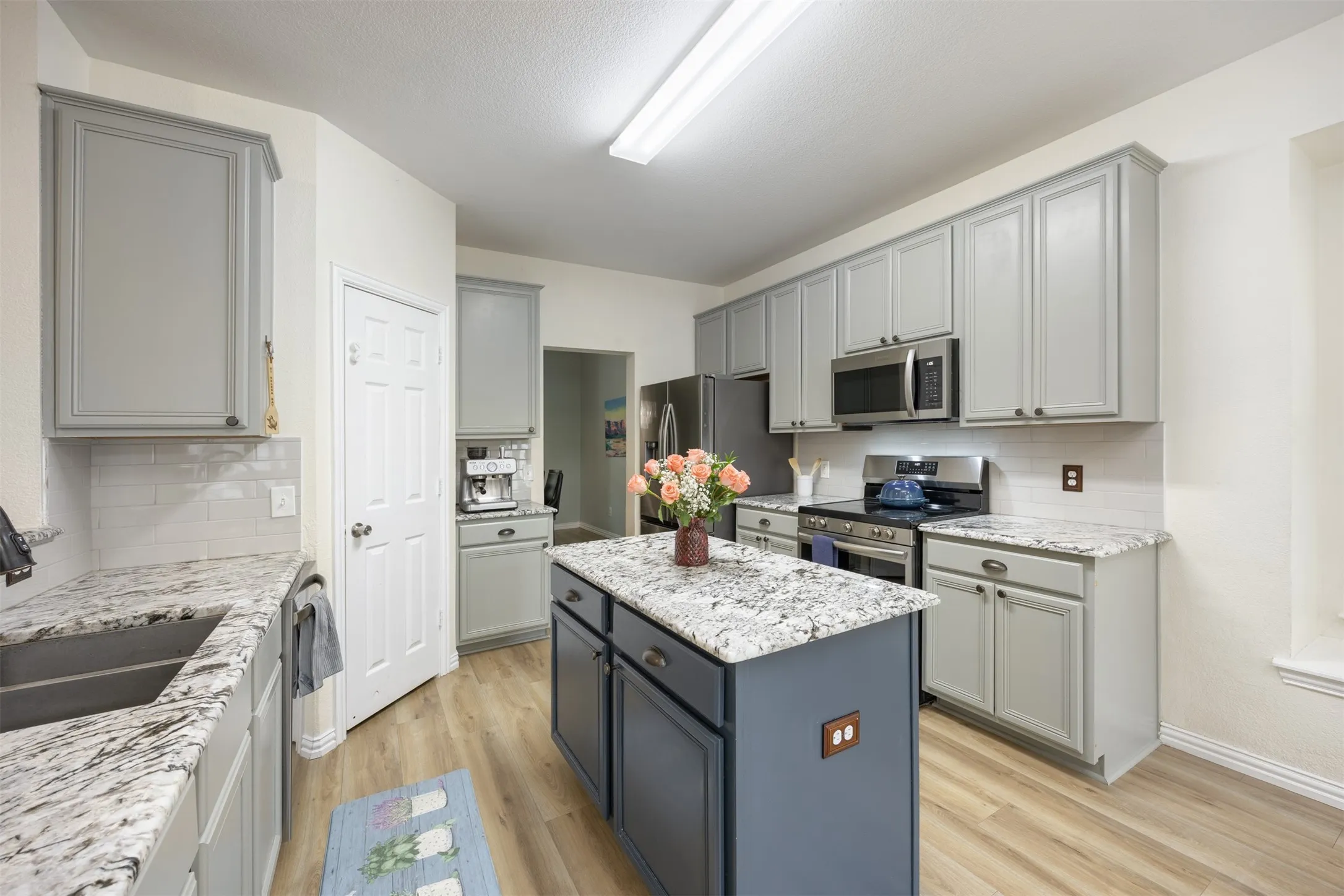 Well-appointed kitchen featuring light-colored cabinetry, stainless steel appliances, granite countertops, and a central island with contrasting cabinetry
