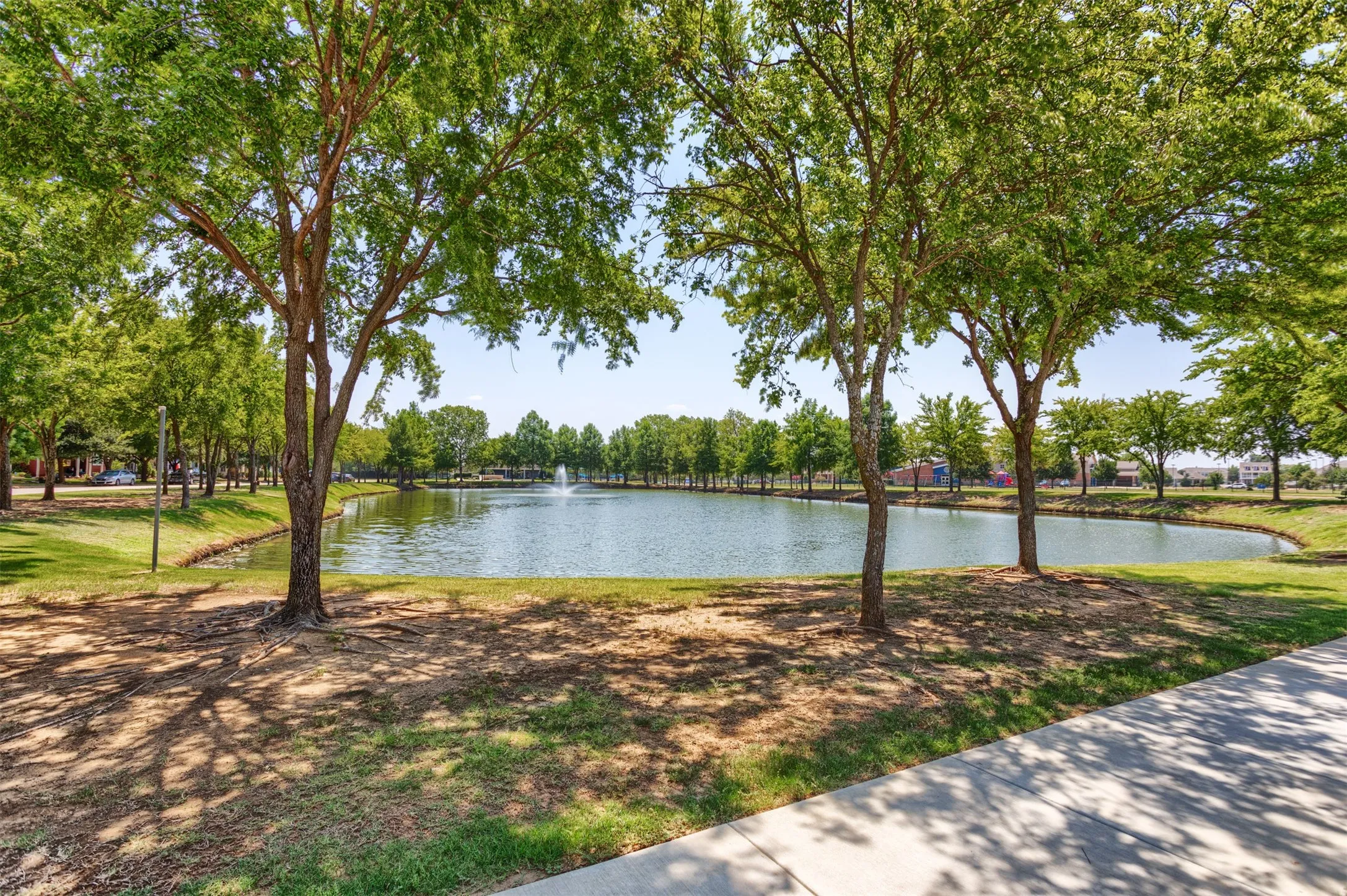 The property features a tranquil lake with a fountain, surrounded by lush green trees and a paved walkway