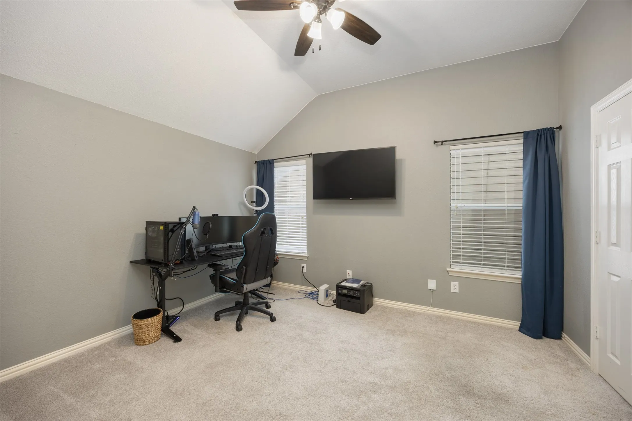 This room features a vaulted ceiling, a ceiling fan with light fixture, and windows with blinds and curtains
