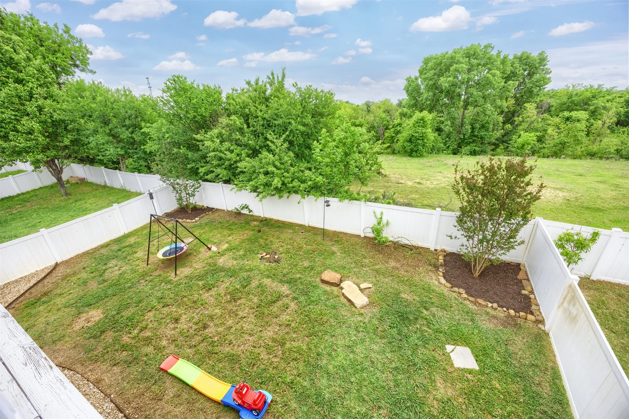 The property features a fenced yard with a lawn, landscaping, and mature trees beyond the fence line