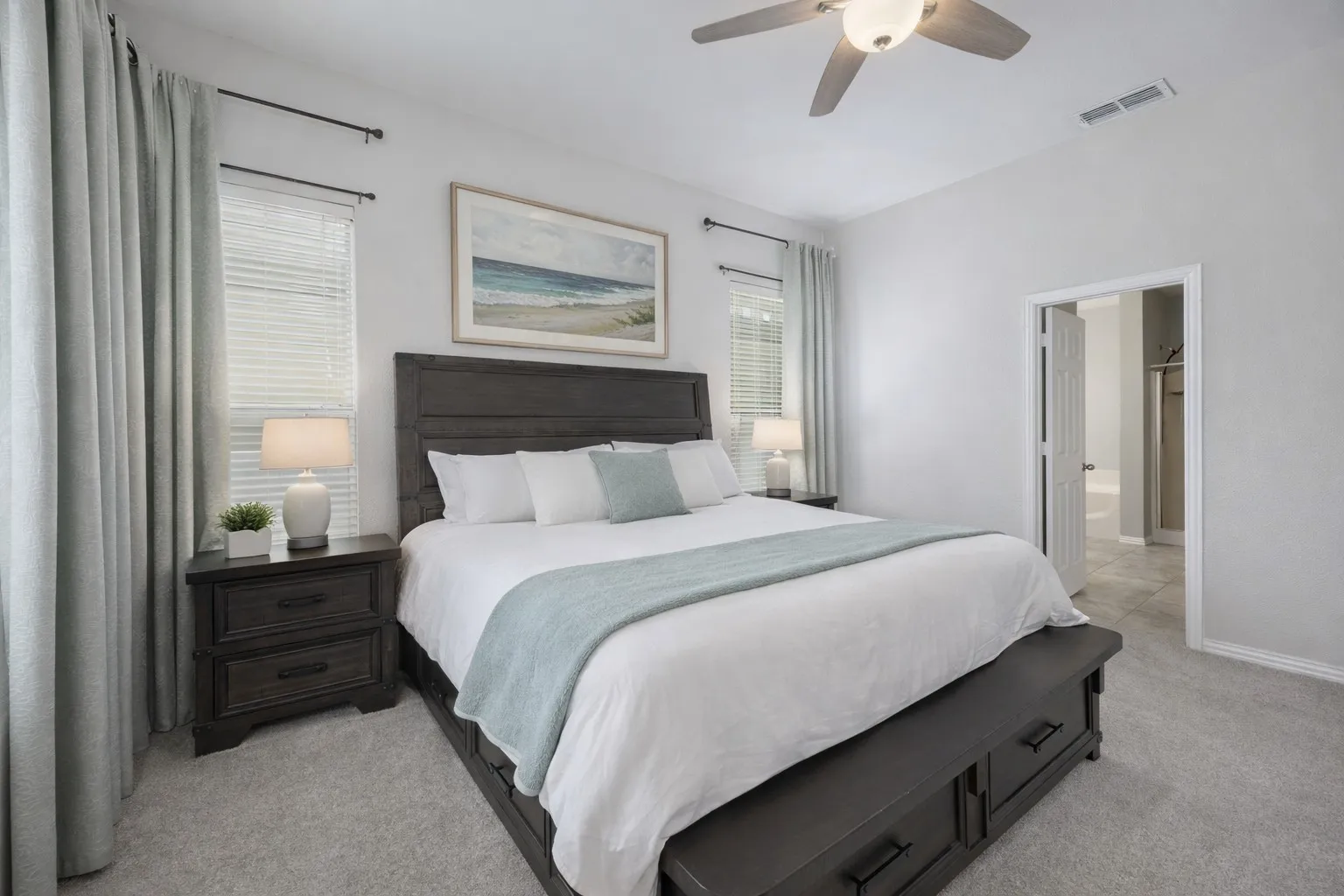 Spacious bedroom featuring light-colored walls, carpeted flooring, a ceiling fan, and large windows with blinds and curtains