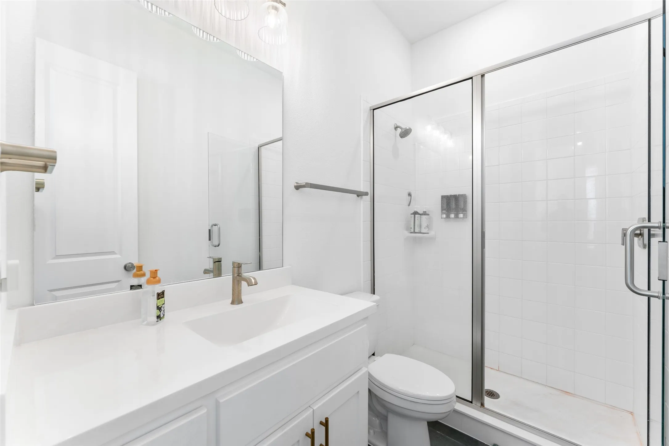 Bathroom featuring a white vanity with a single basin sink, a large mirror, and a glass-enclosed shower with white tiled walls