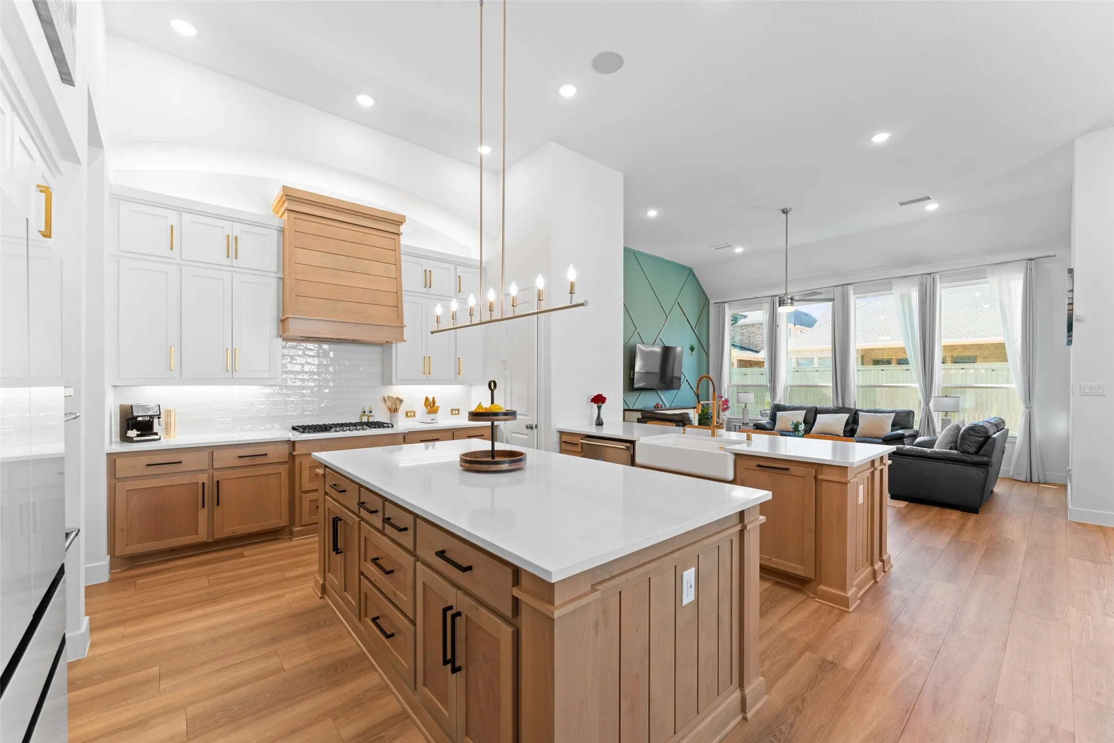 The kitchen features a large island with a white countertop and natural wood cabinetry, a white subway tile backsplash, and a gold-toned chandelier