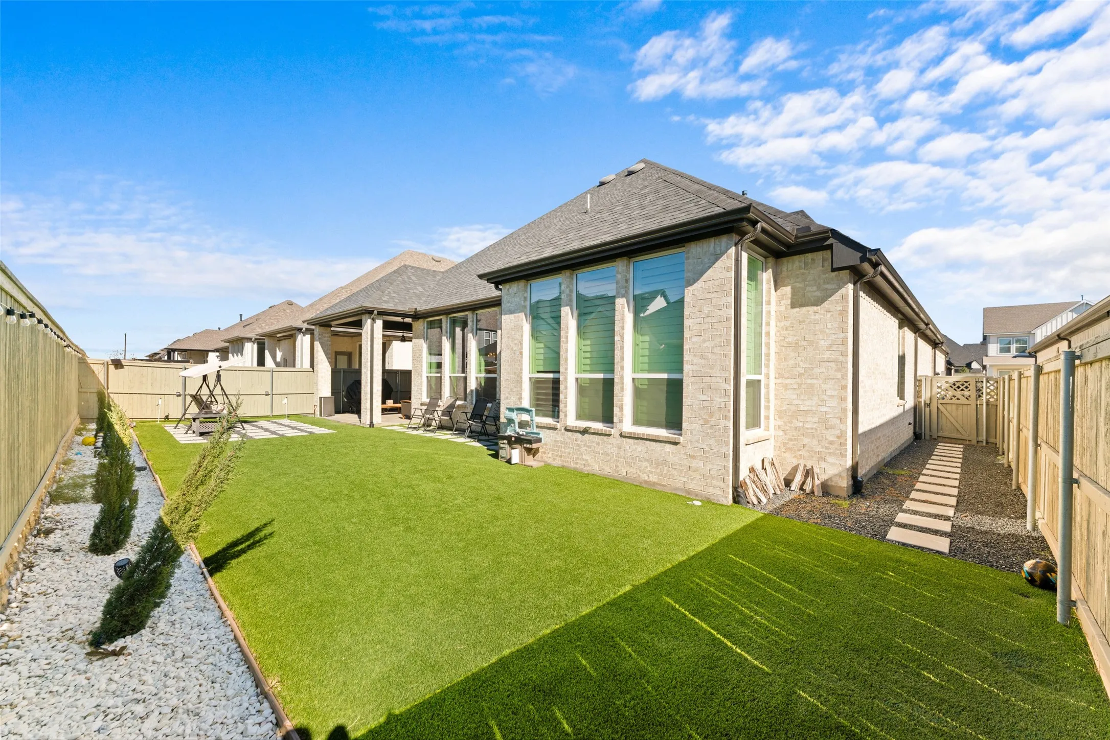 The property features a spacious backyard with artificial turf, a rock border with planted shrubs, and a paved patio area
