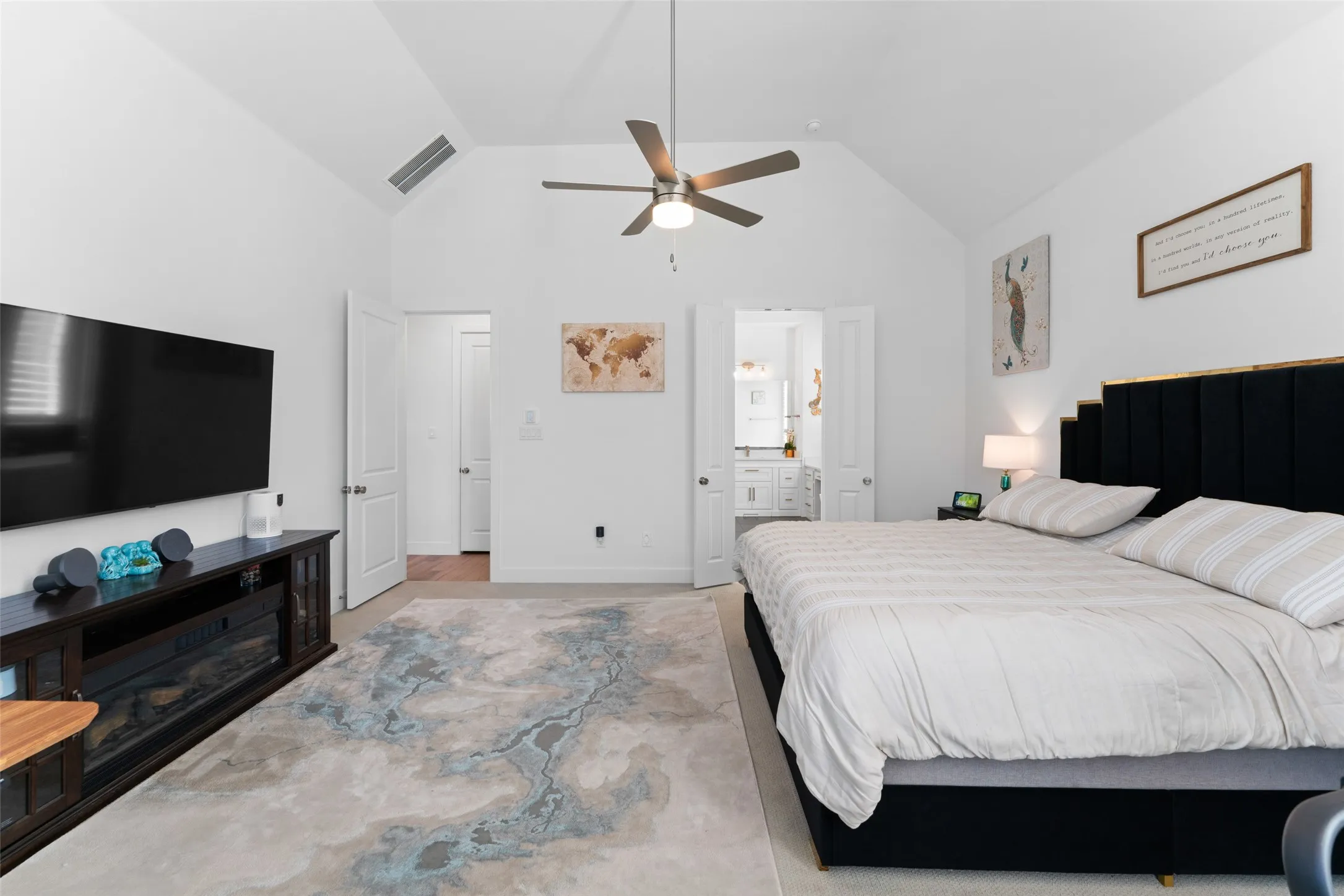 This room features vaulted ceilings, a ceiling fan, and a light-colored rug with a distinct pattern