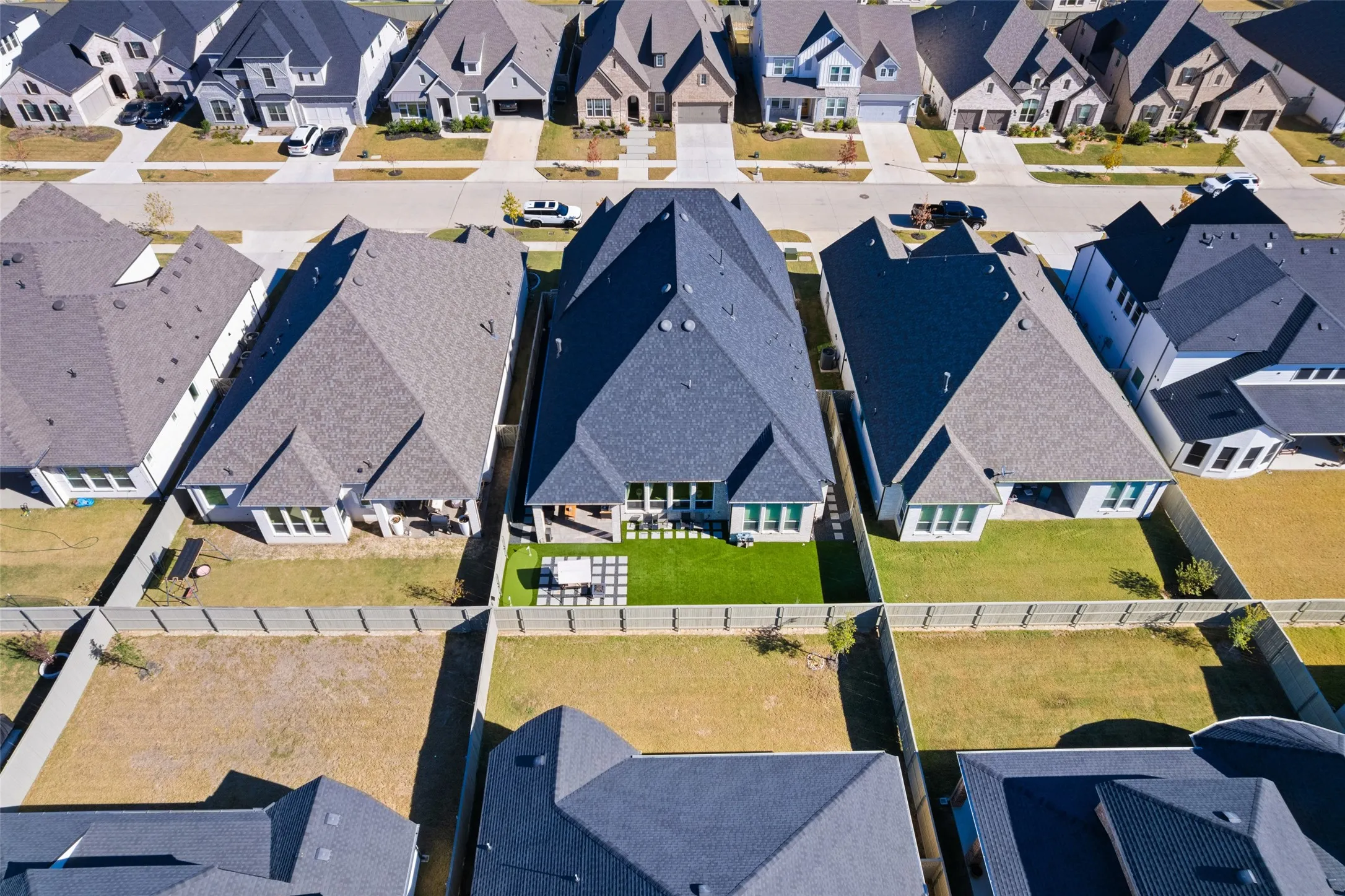 Aerial view showcasing a residential property with a dark grey roof and a fenced backyard featuring a patio area and a lawn