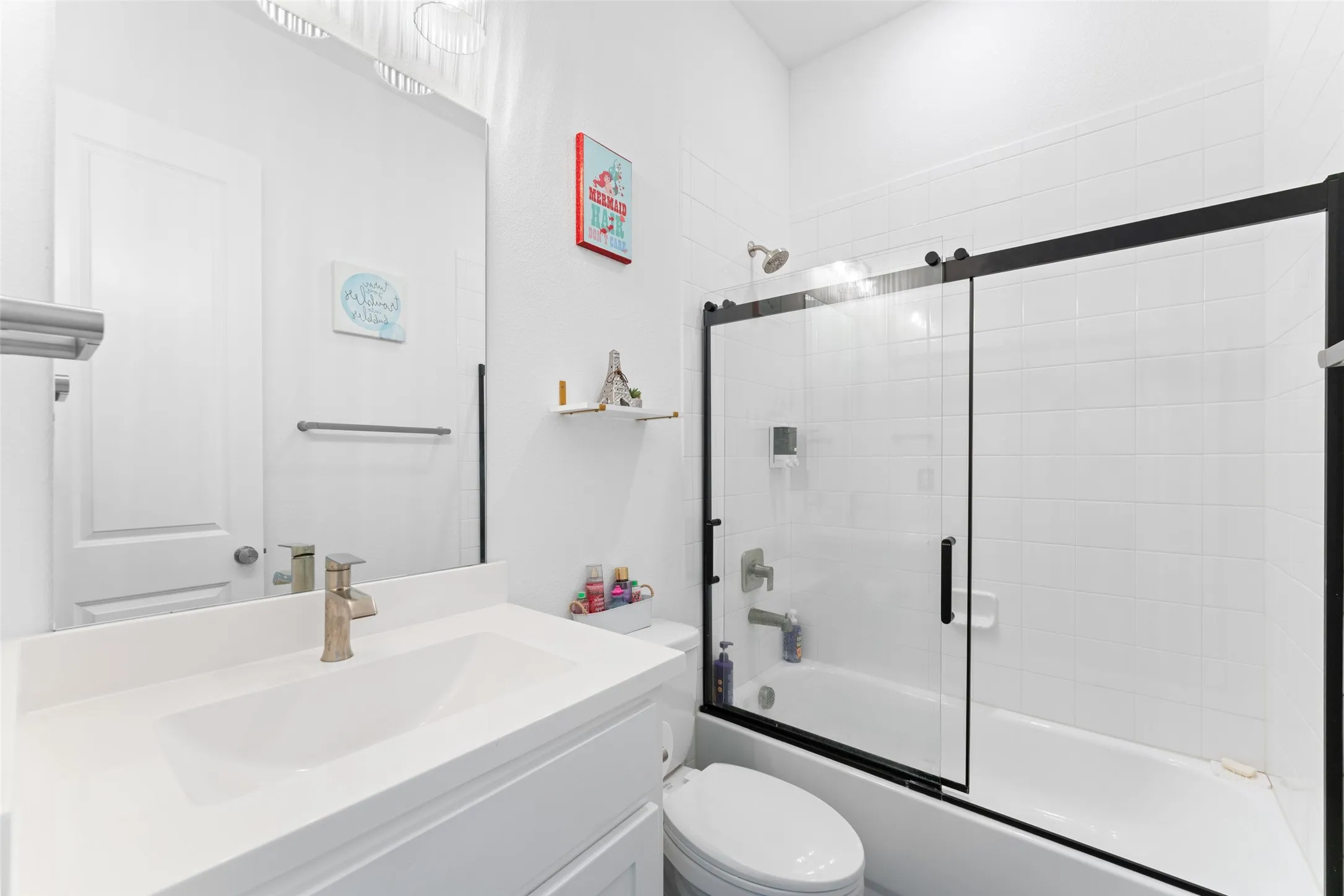 Bathroom featuring a vanity with a white countertop and an integrated sink, a large mirror, and a bathtub with a black-framed glass sliding door