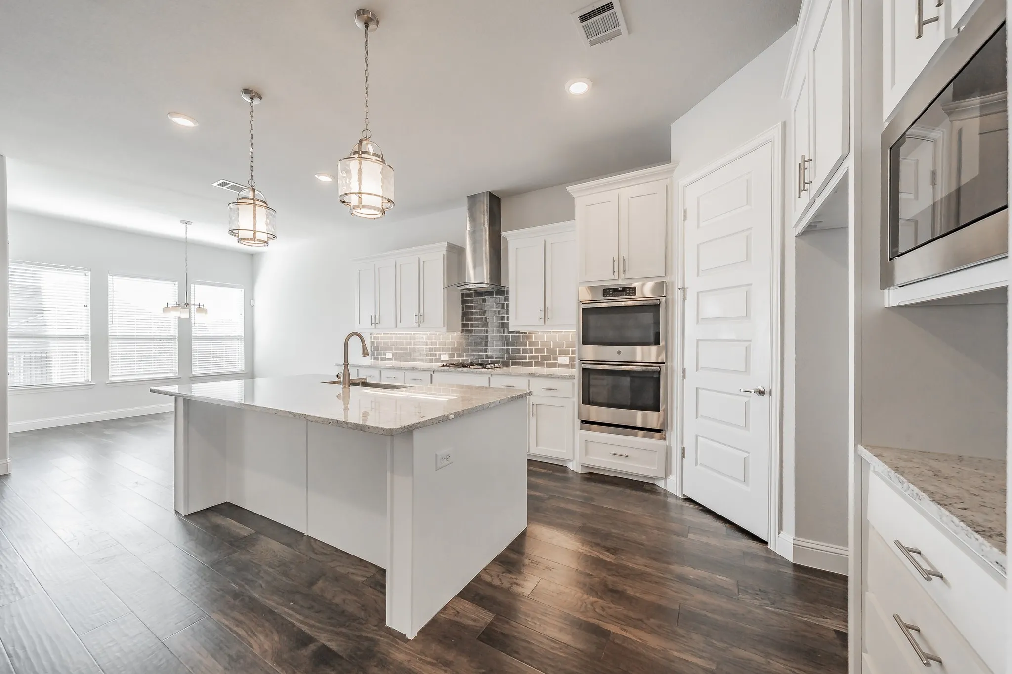 Kitchen featuring light stone countertops, stainless steel appliances, decorative light fixtures, backsplash, and a center island with sink