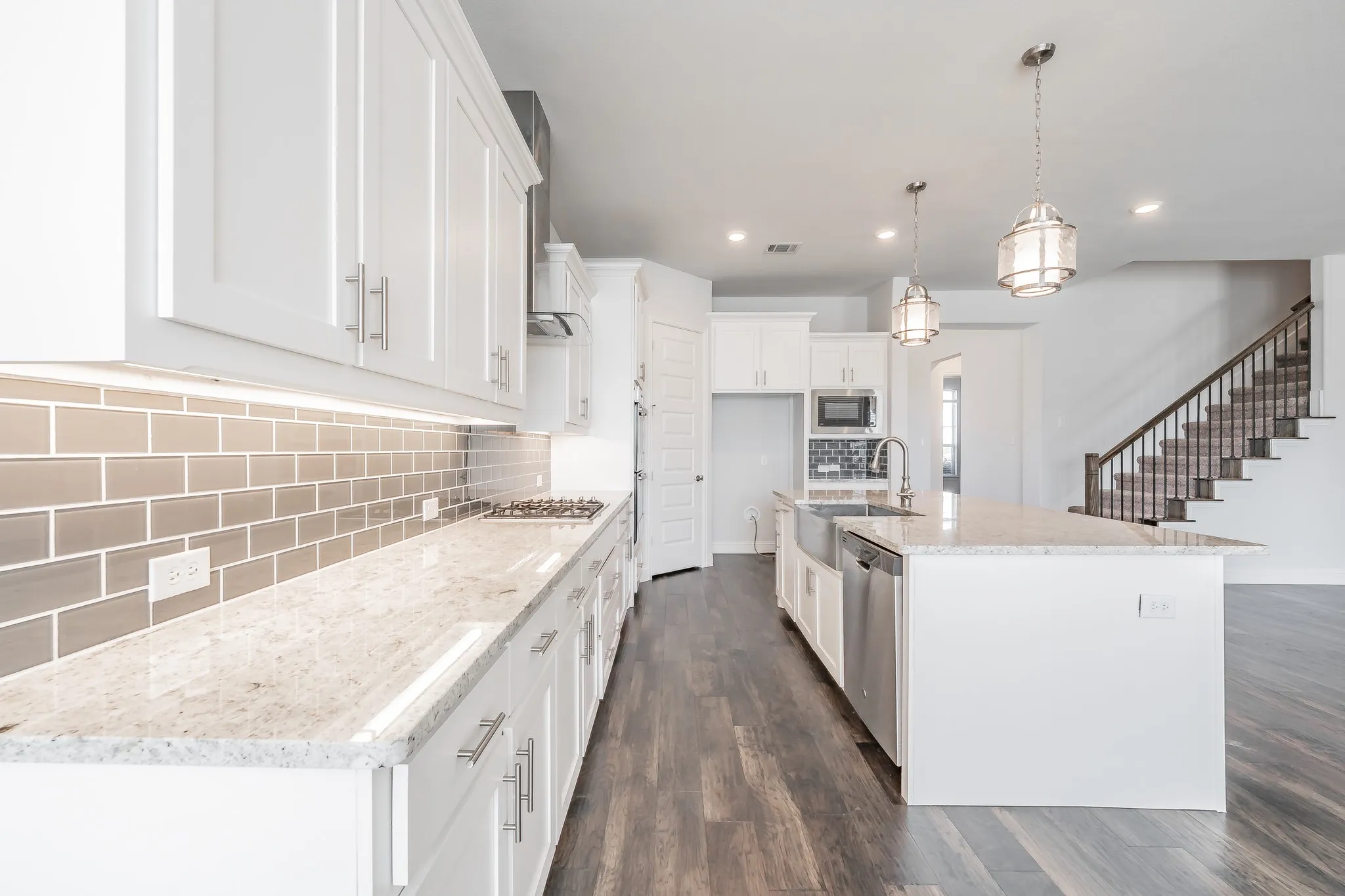 Kitchen with backsplash, light stone counters, a center island with sink, dark wood finished floors, and decorative light​​‌​​​​‌​​‌‌​‌‌​​​‌‌​‌​‌​‌​​​‌​​ fixtures