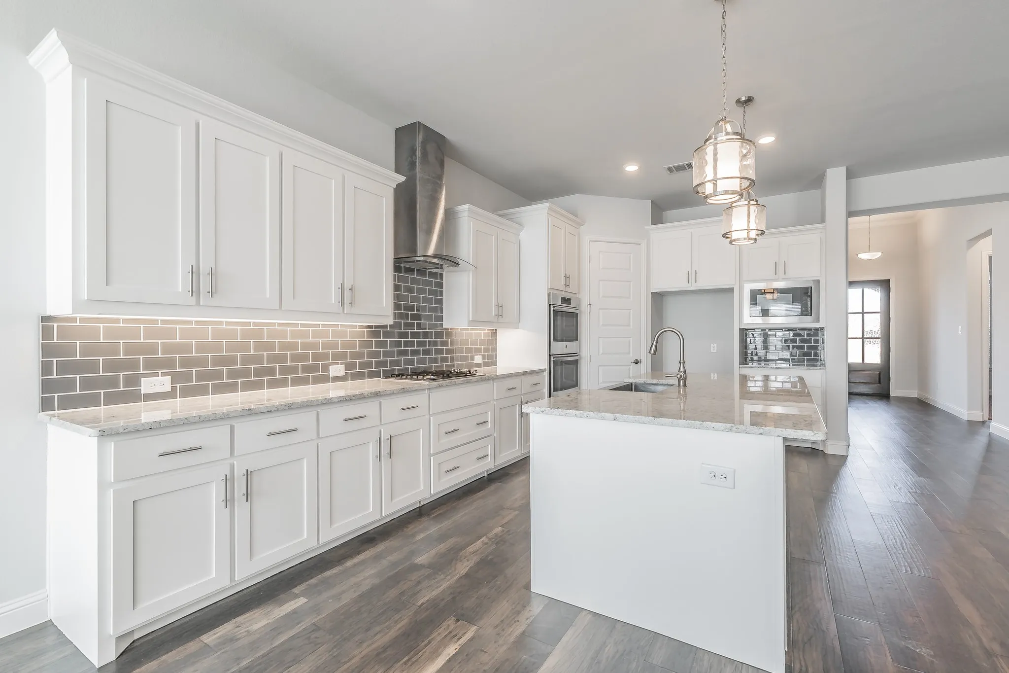 Kitchen featuring light stone countertops, backsplash, a center island with sink, white cabinets, and hanging light fixtures