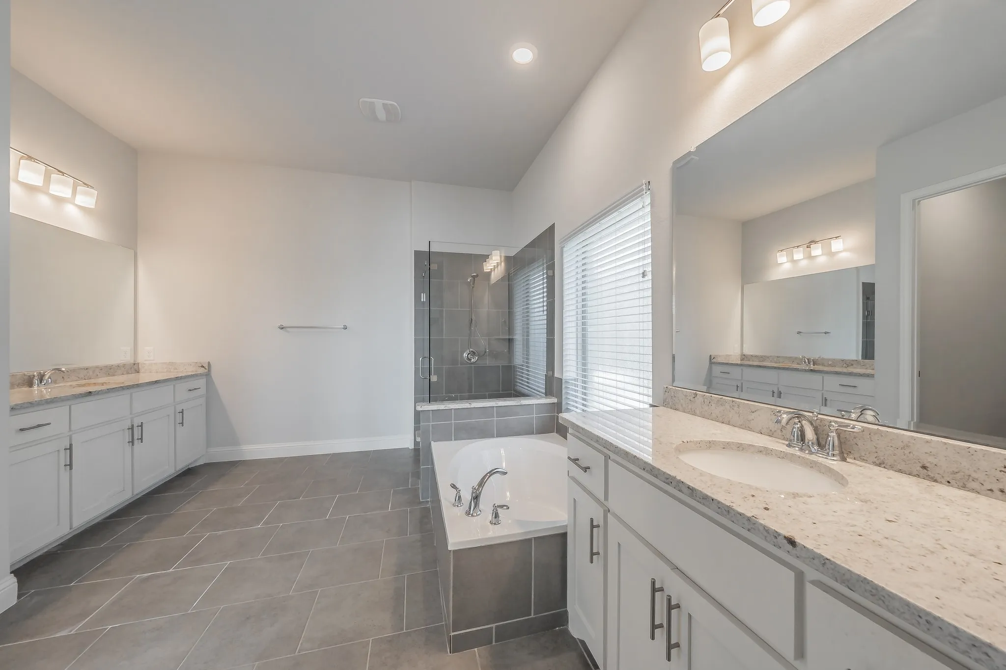 Bathroom featuring two vanities, a bath, a shower stall, dark tile patterned floors, and recessed lighting