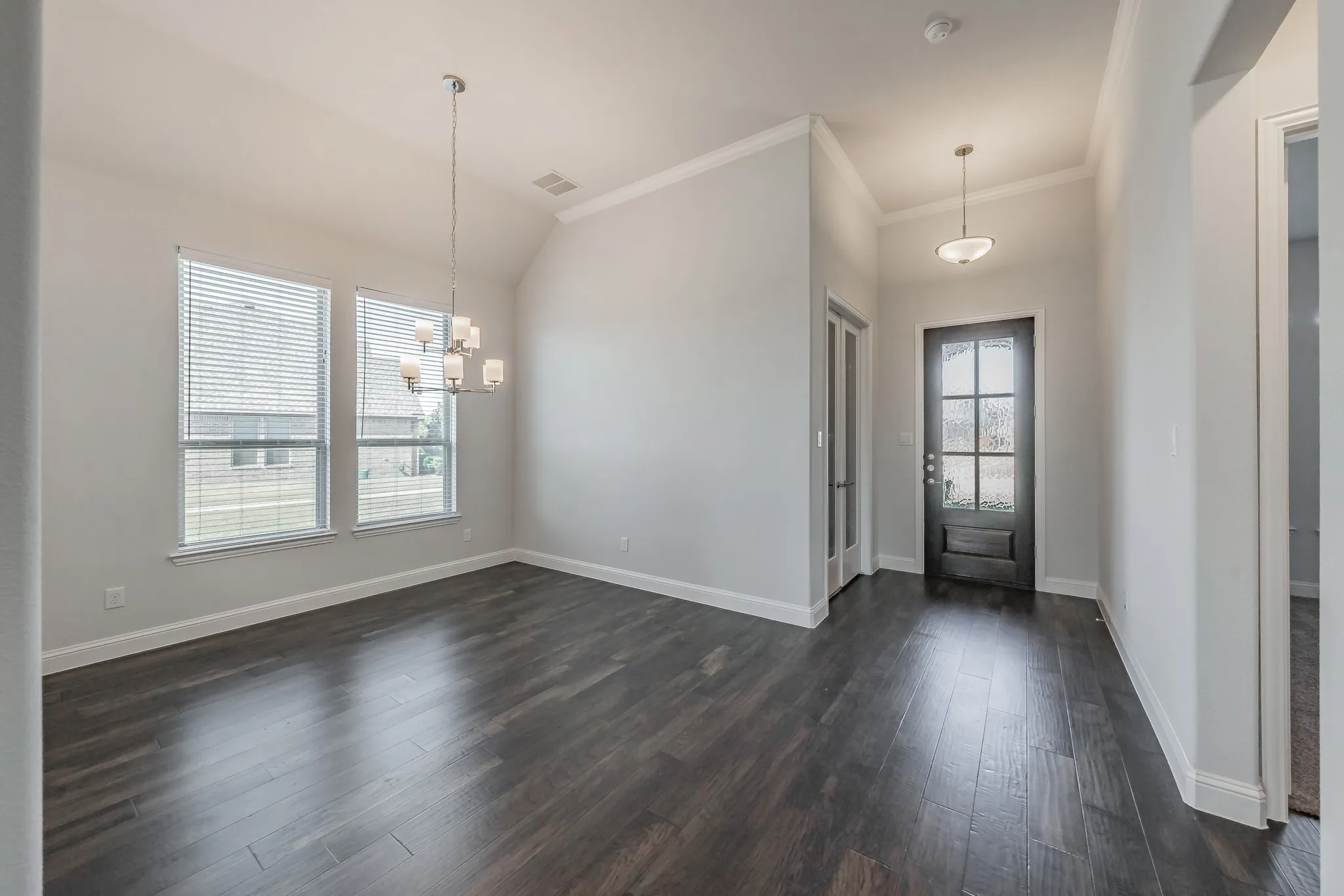 Entrance foyer with a chandelier, dark wood-style flooring, crown molding, and vaulted ceiling