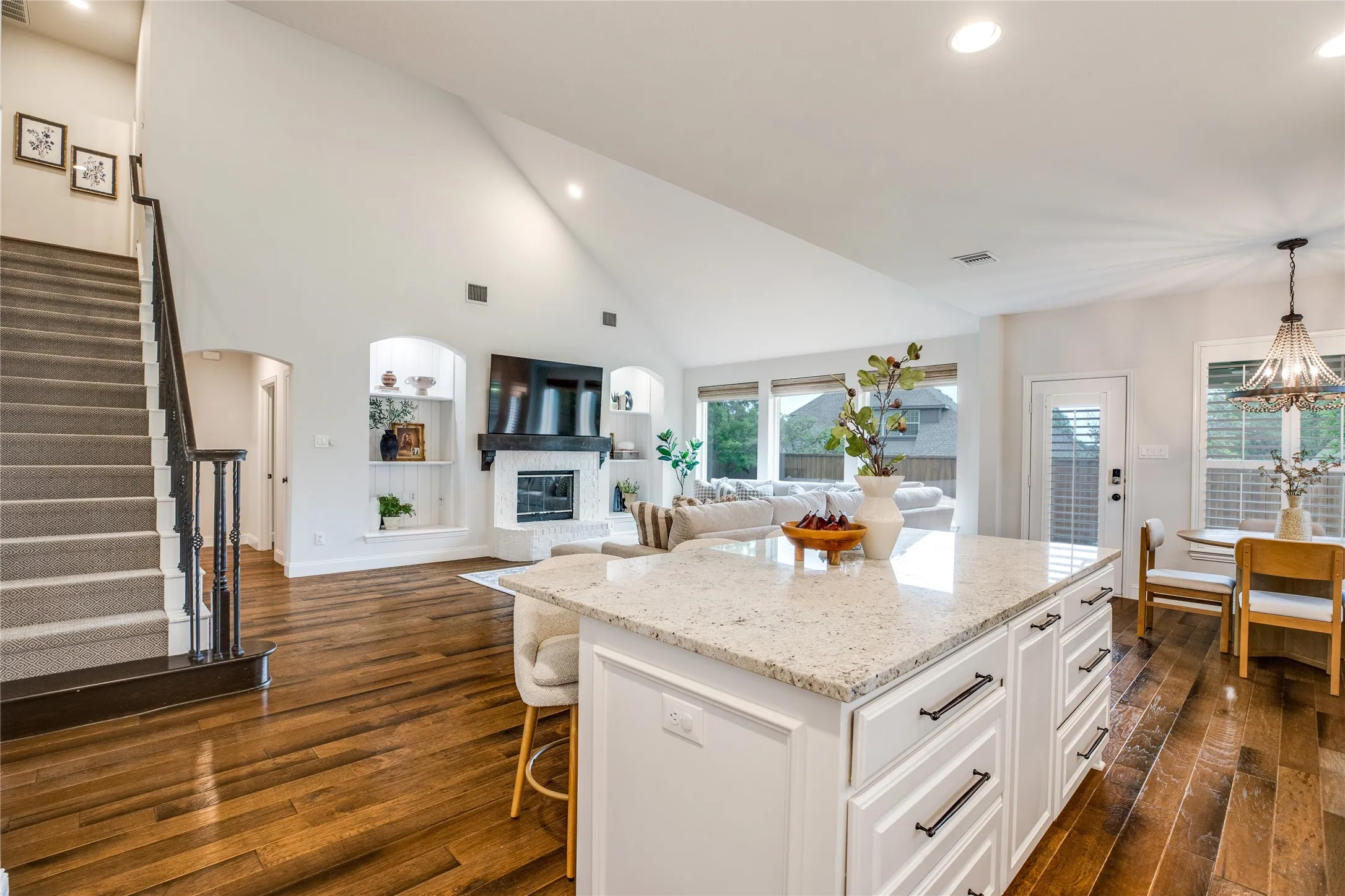 Open concept living area featuring hardwood floors, a kitchen island with a light-colored countertop, and a living room with a fireplace and large windows