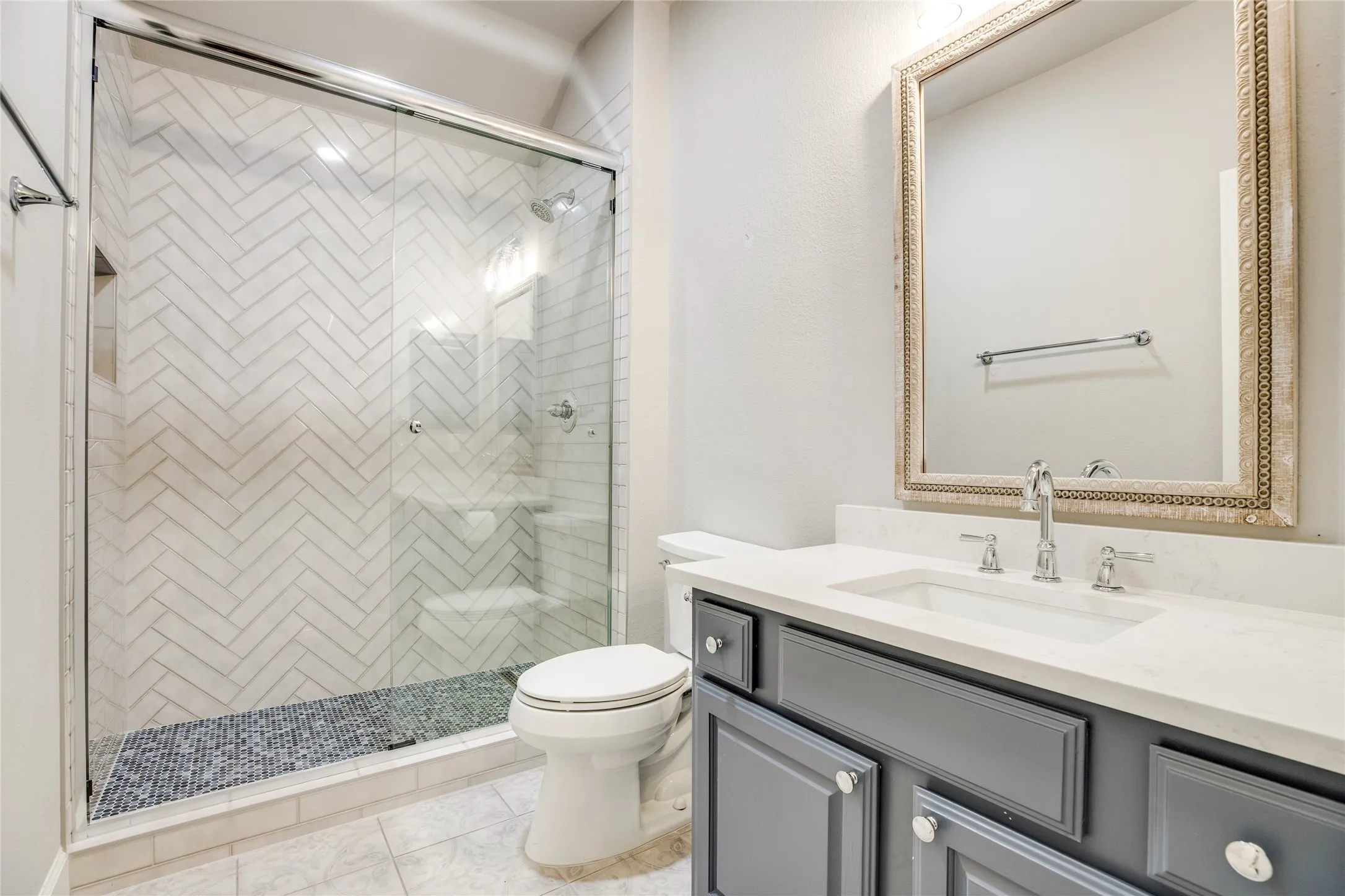 The bathroom features a glass-enclosed shower with herringbone tile work and a pebble-style floor