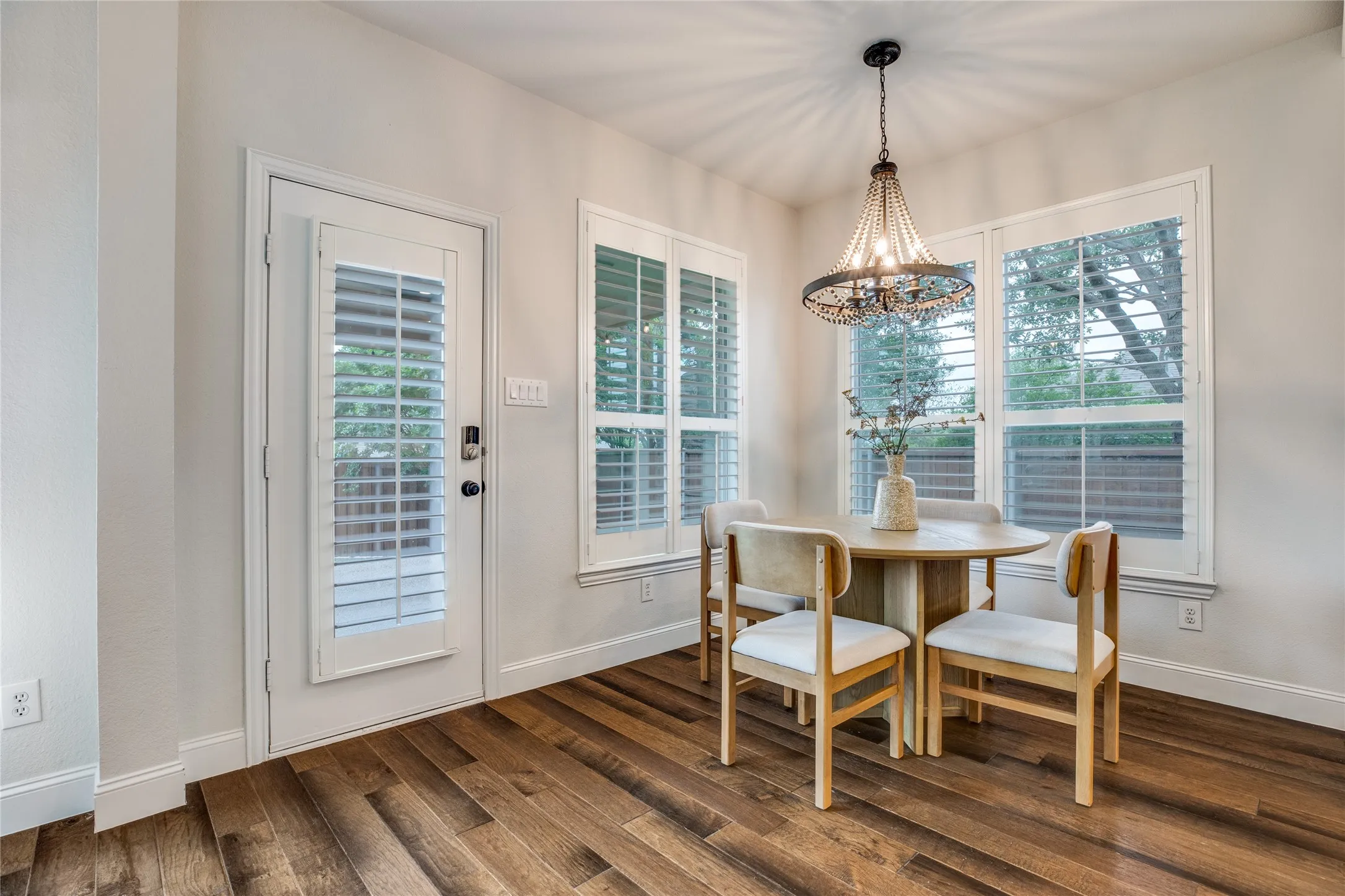 Dining area featuring rich hardwood floors, an elegant chandelier, and windows fitted with white plantation shutters