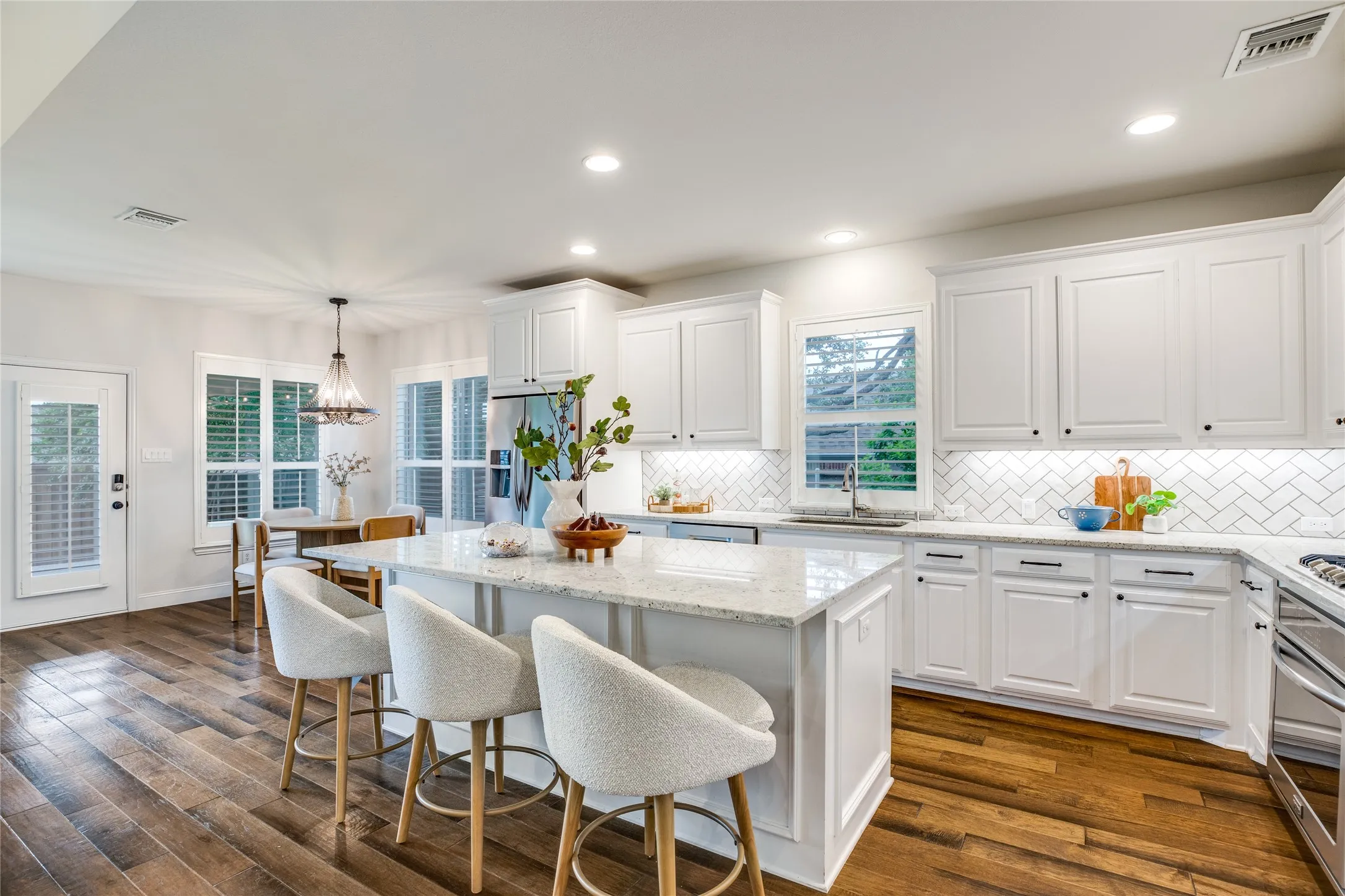 The property features a kitchen with white cabinetry, a large kitchen island with a light-colored countertop, and hardwood floors