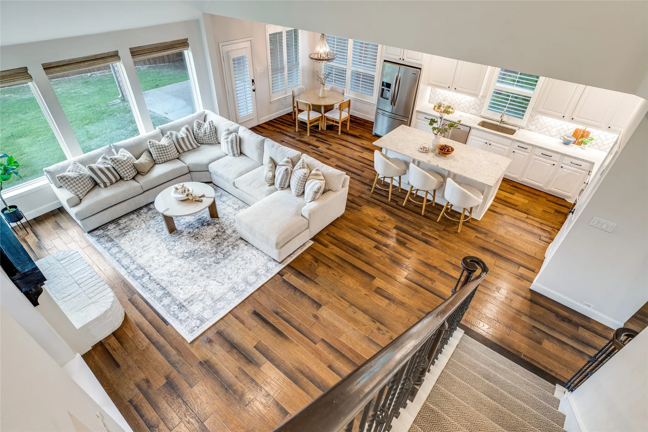 Open concept living space with hardwood floors throughout the main areas, featuring a kitchen with white cabinetry, a large island with seating, and a stainless steel refrigerator