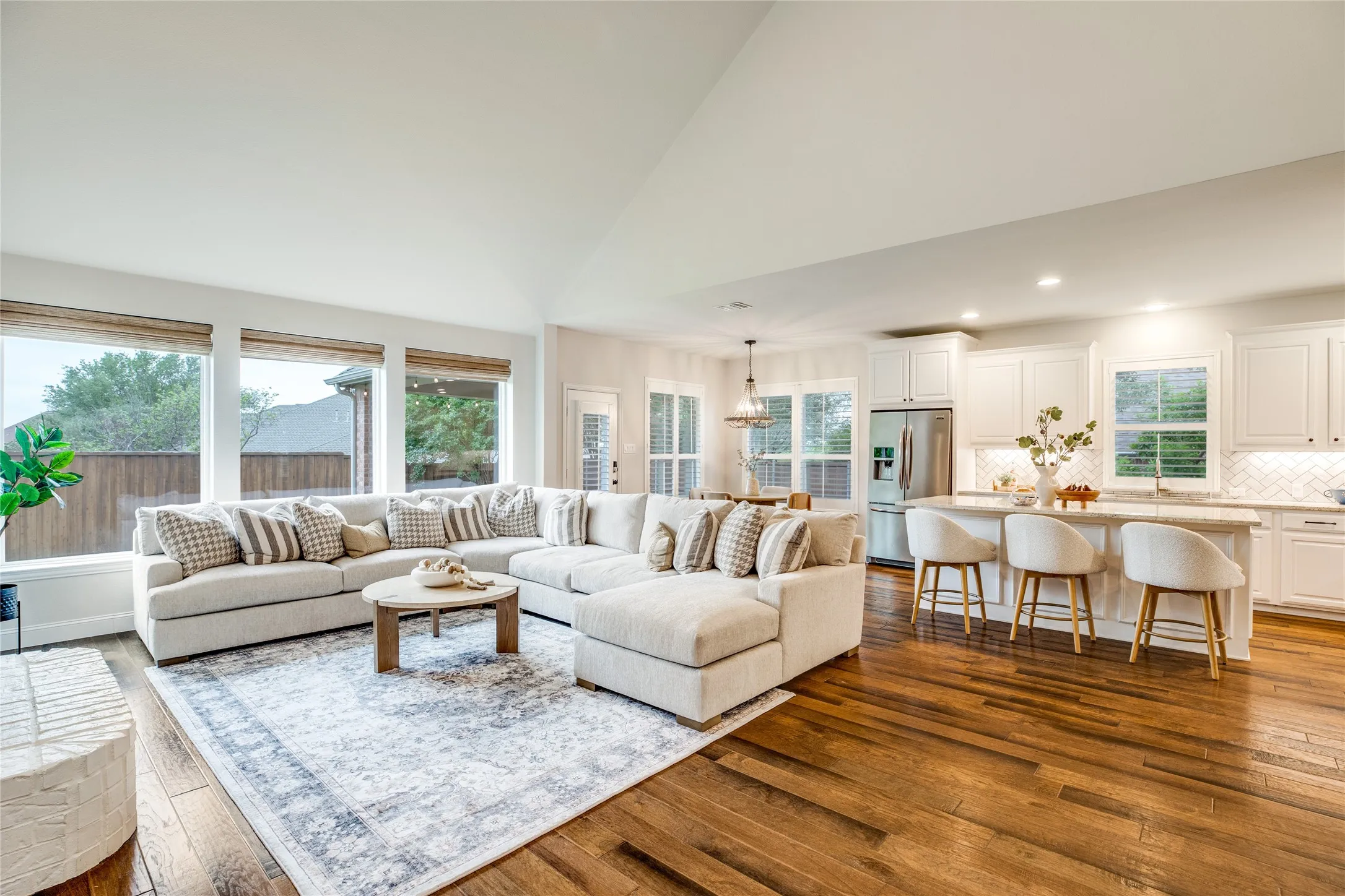 The expansive living area features rich hardwood flooring, a large area rug, and an abundance of natural light from several windows
