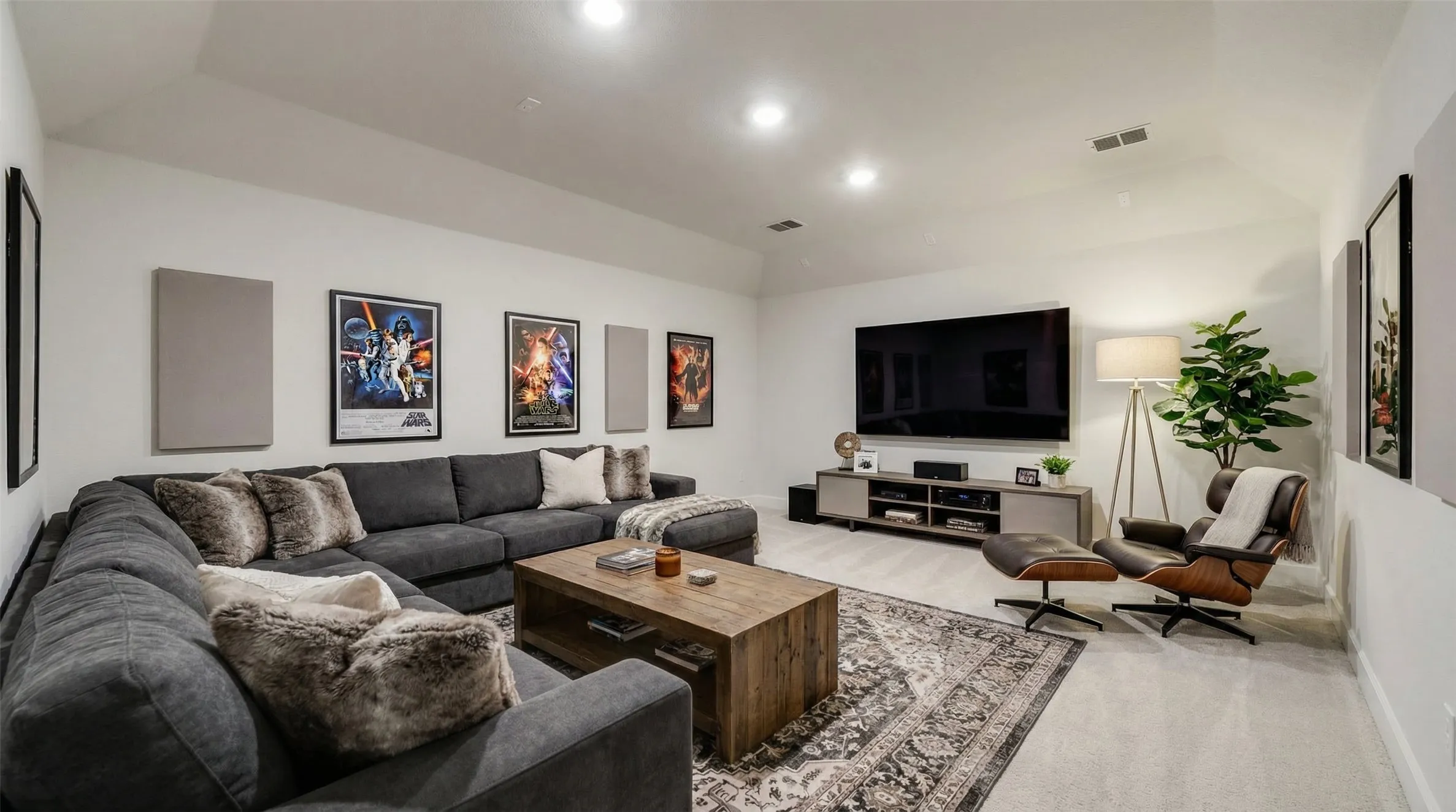 Spacious living area featuring light-colored carpeting, recessed lighting, and a large wall-mounted television