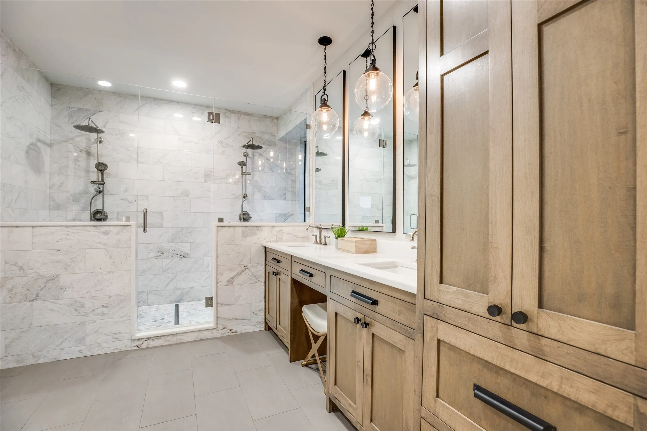 This bathroom features a double vanity with light wood cabinetry, white countertops, and circular pendant lighting